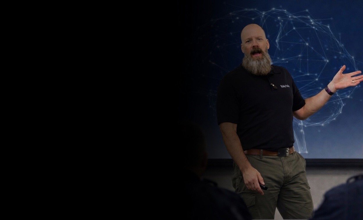 Instructor presenting Rally Point law enforcement training in a controlled classroom environment, wearing a black polo and khaki pants, delivering instruction in front of a law enforcement officers.