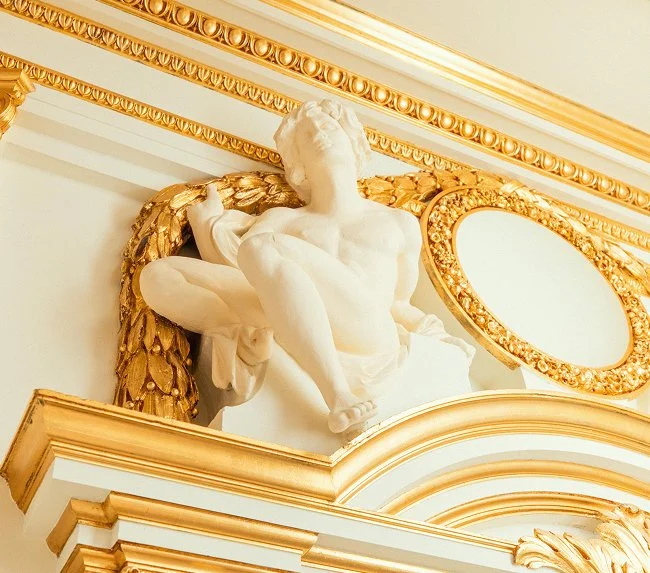 Eine weiße Skulptur eines menschlichen Körpers mit goldverzierten Elementen an einer Wand im Barockstil. Renaissance-Statue aus weißem Marmor im Kaisersaal als dekoratives Element und Hinweis auf den Kursstandort.