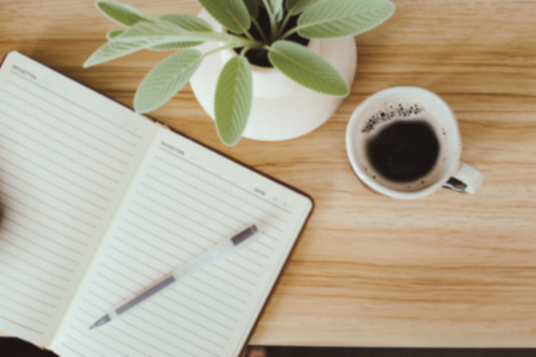 Open notebook with a pen, a potted green plant, a cup of black coffee, on a wooden table.