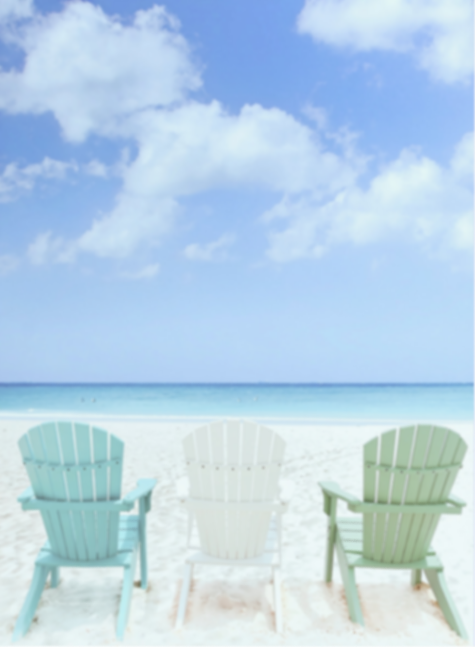 Three colorful Adirondack chairs on a beach with sand, ocean, blue sky, and clouds.