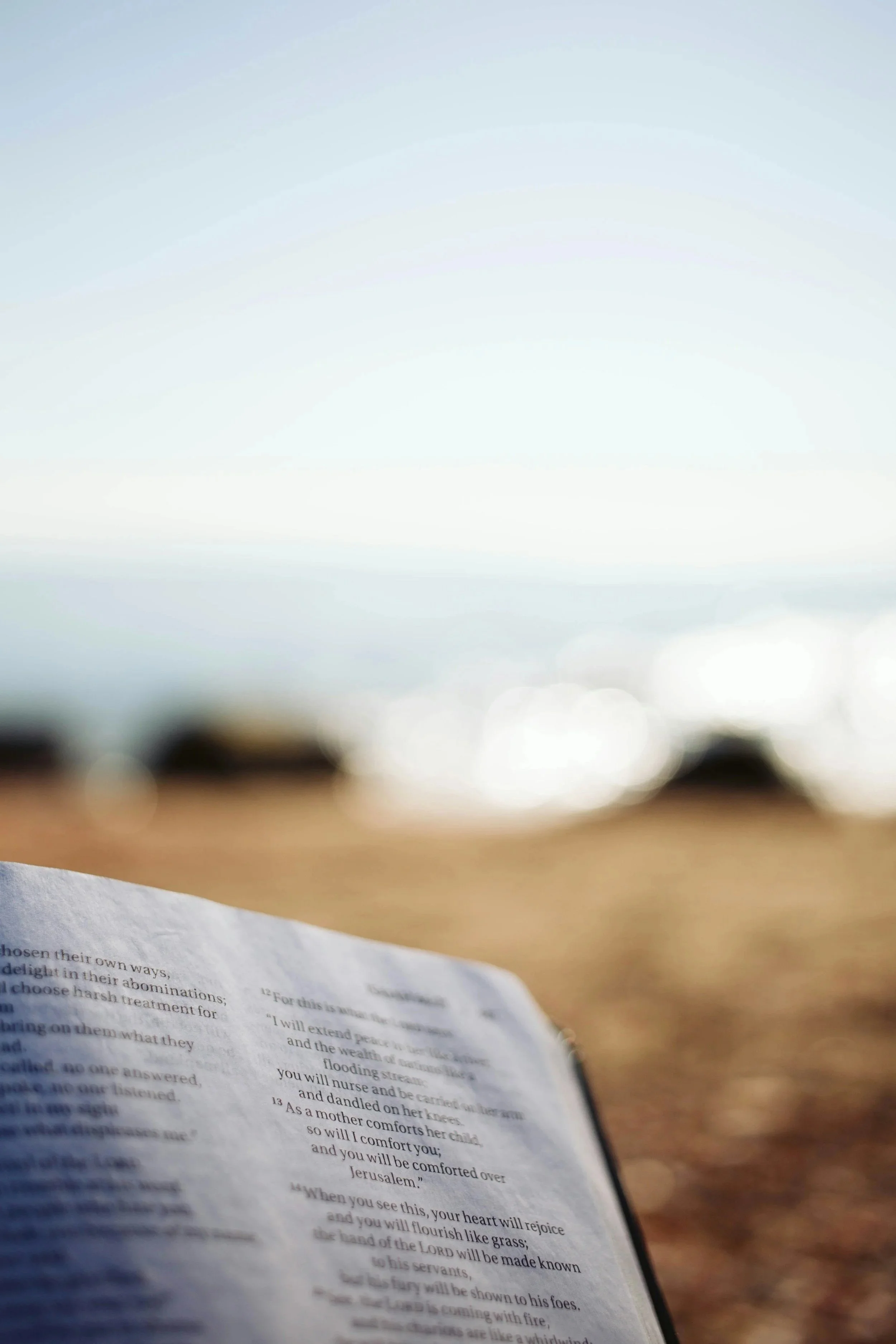 A blurry view of a printed page, likely a book or document, on a surface with an out-of-focus background that appears to be an outdoor scene with a clear sky.
