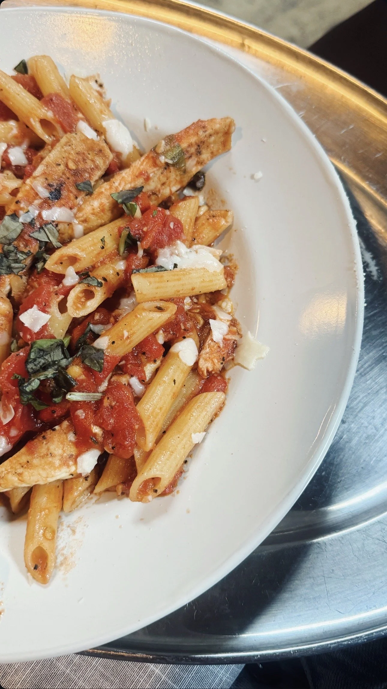Pasta with tomato sauce, chicken, herbs, and cheese in a white bowl.