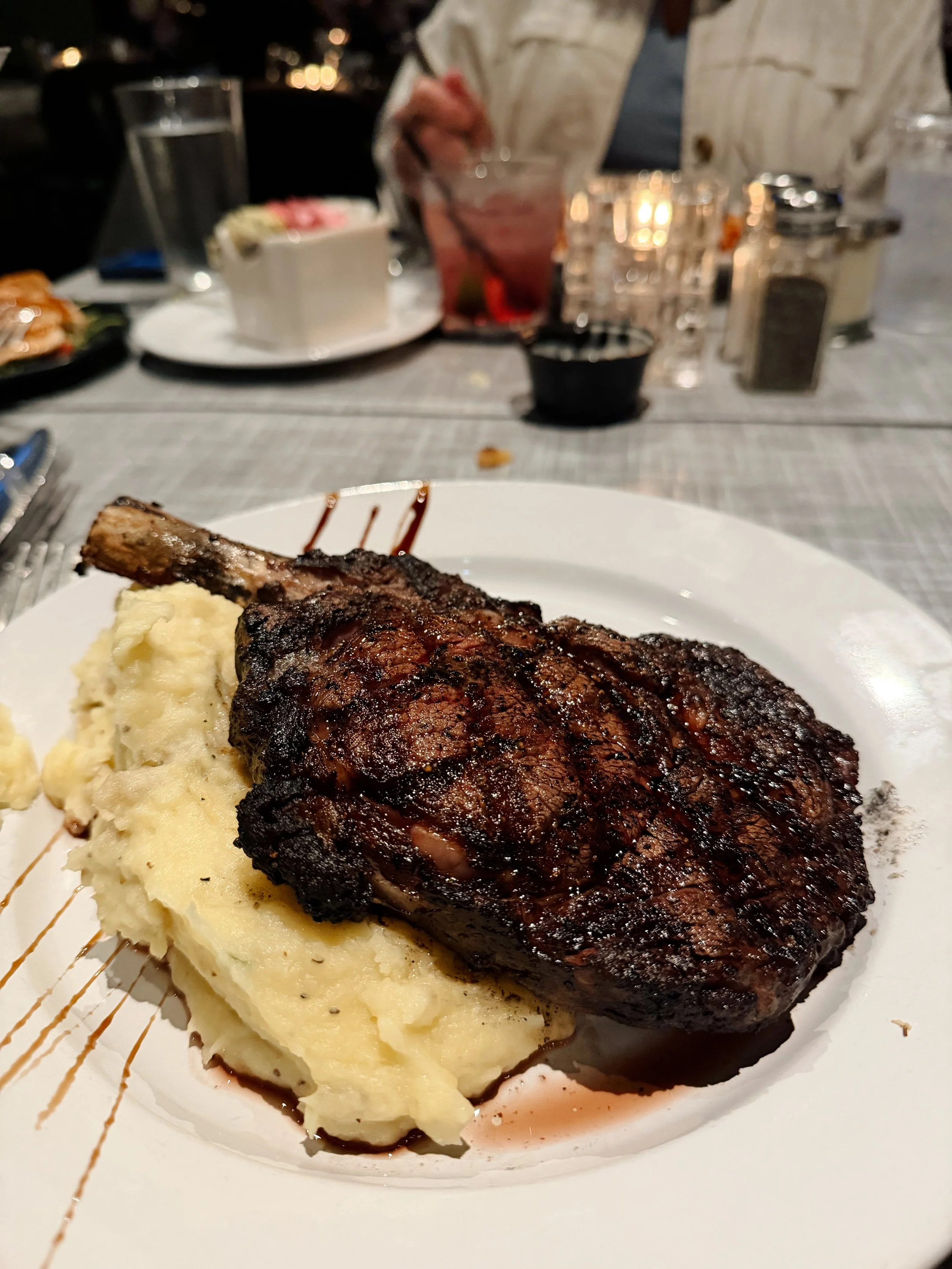 Grilled steak with mashed potatoes on a white plate in a restaurant setting.