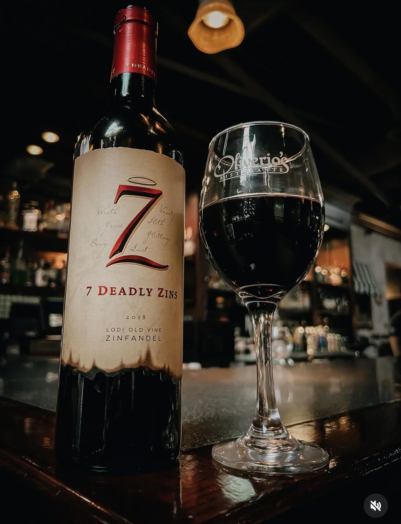 A bottle of Zinfandel red wine and a glass of red wine on a bar counter inside a dimly lit restaurant.