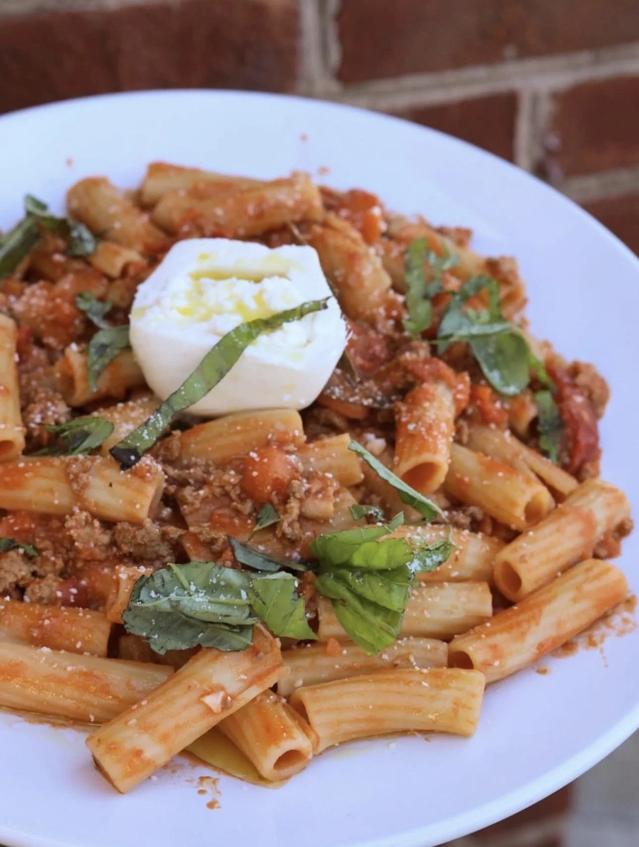 Plate of pasta penne with tomato sauce, garnished with basil leaves.