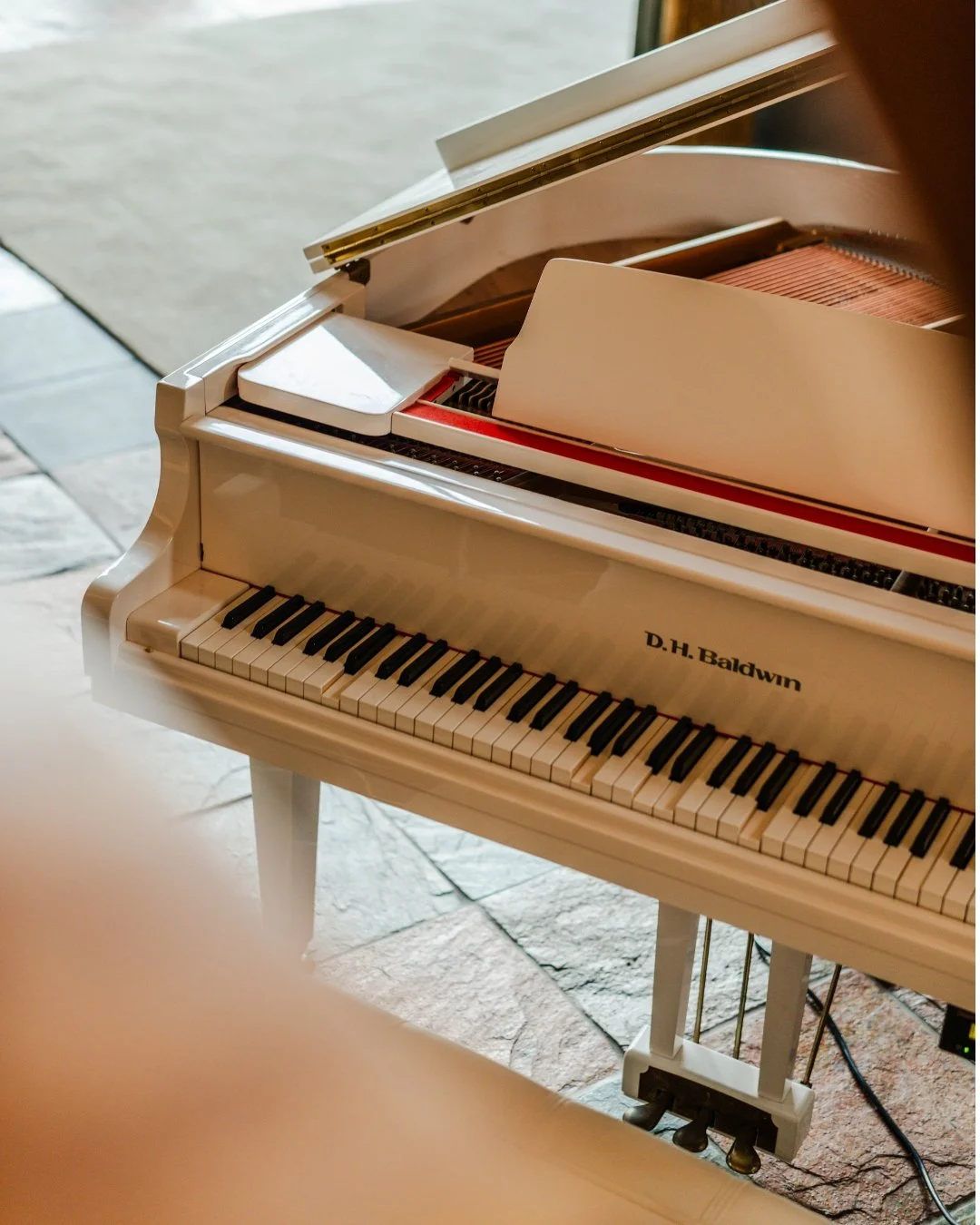White grand piano with D. H. Baldwin label, open lid, on a stone floor.