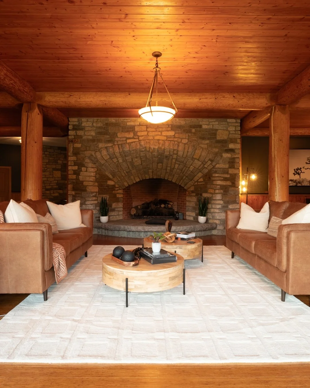 Living room with two brown sofas, a white rug, and a stone fireplace with logs, decorated with potted plants and modern lighting fixtures in woodmont manor groom's suite