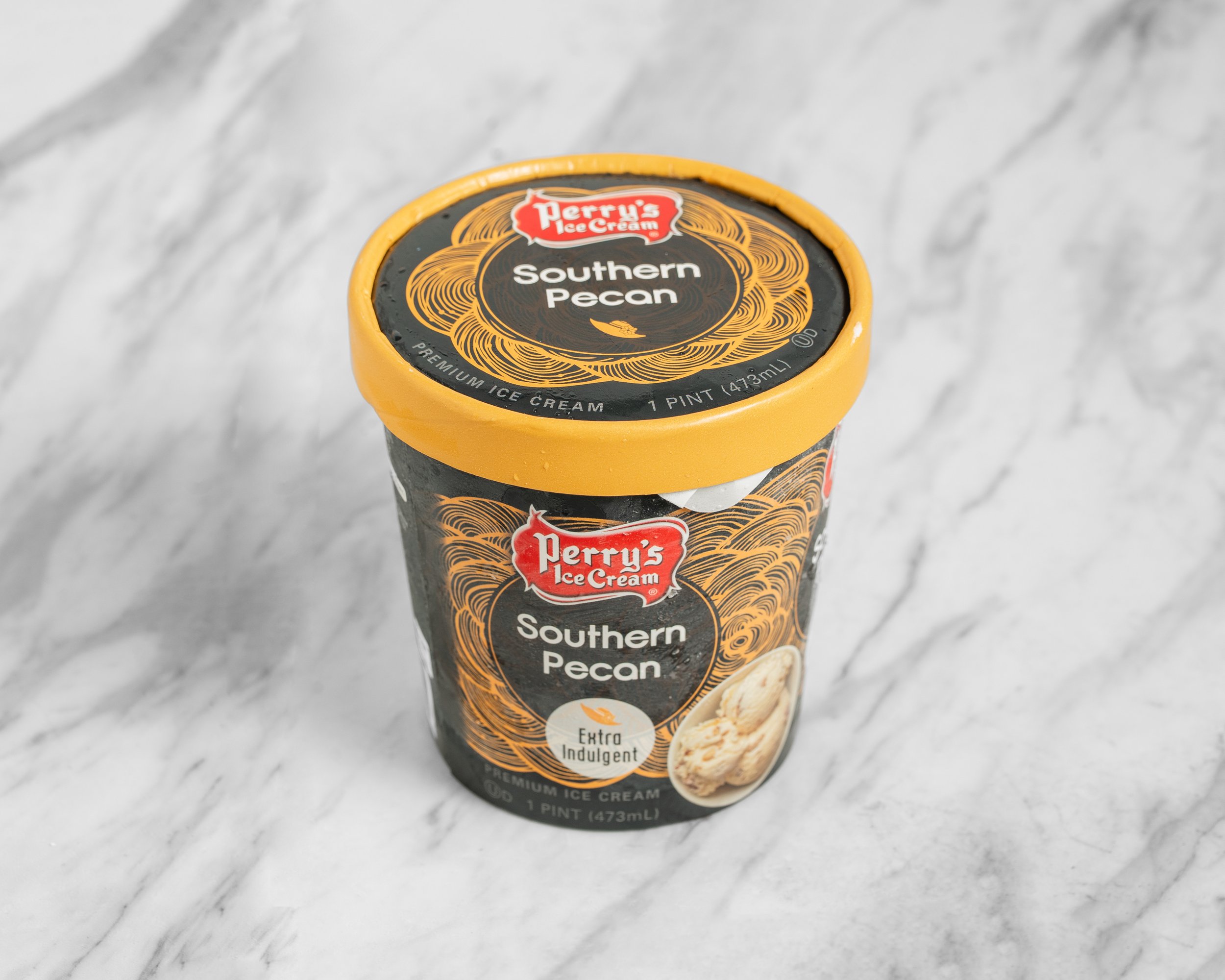 A pint container of Perry's Ice Cream Southern Pecan flavor on a marble surface.