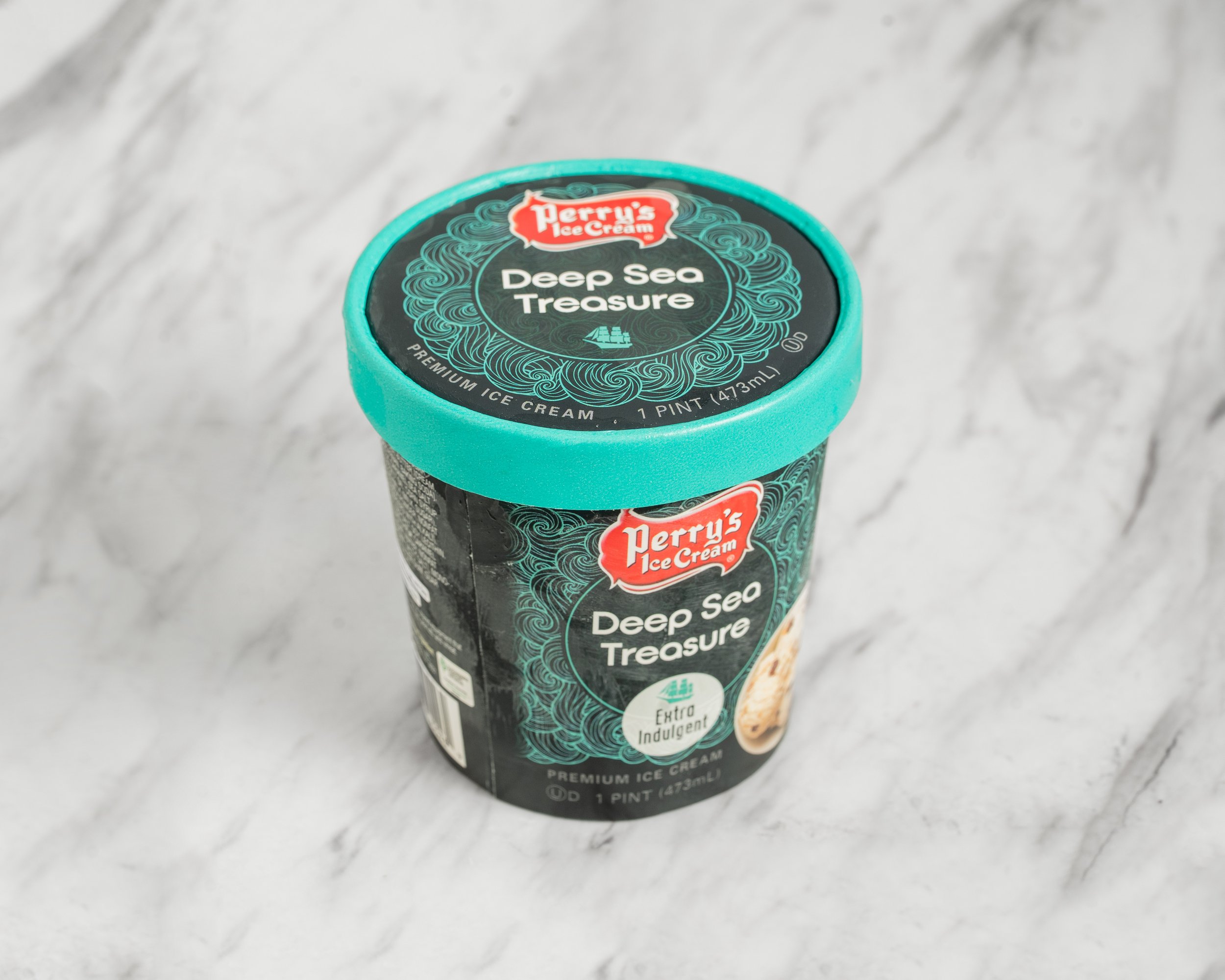 A pint container of Perry's Ice Cream, flavor Deep Sea Treasure, with a turquoise lid and black label, on a marble surface.