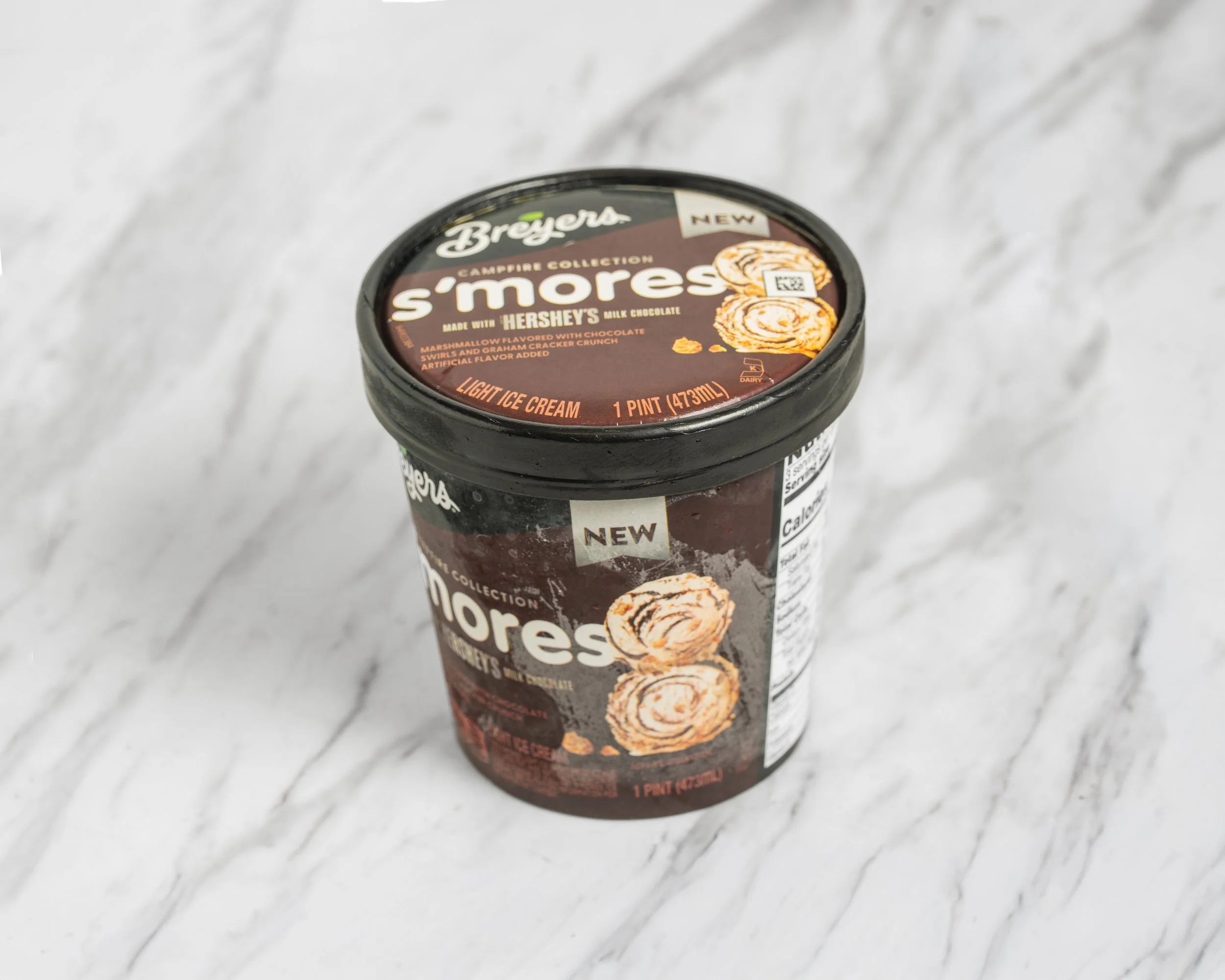 A pint of Breyers S'mores ice cream on a marble surface, featuring chocolate, marshmallow, graham cracker flavors, and a swirl of chocolate.