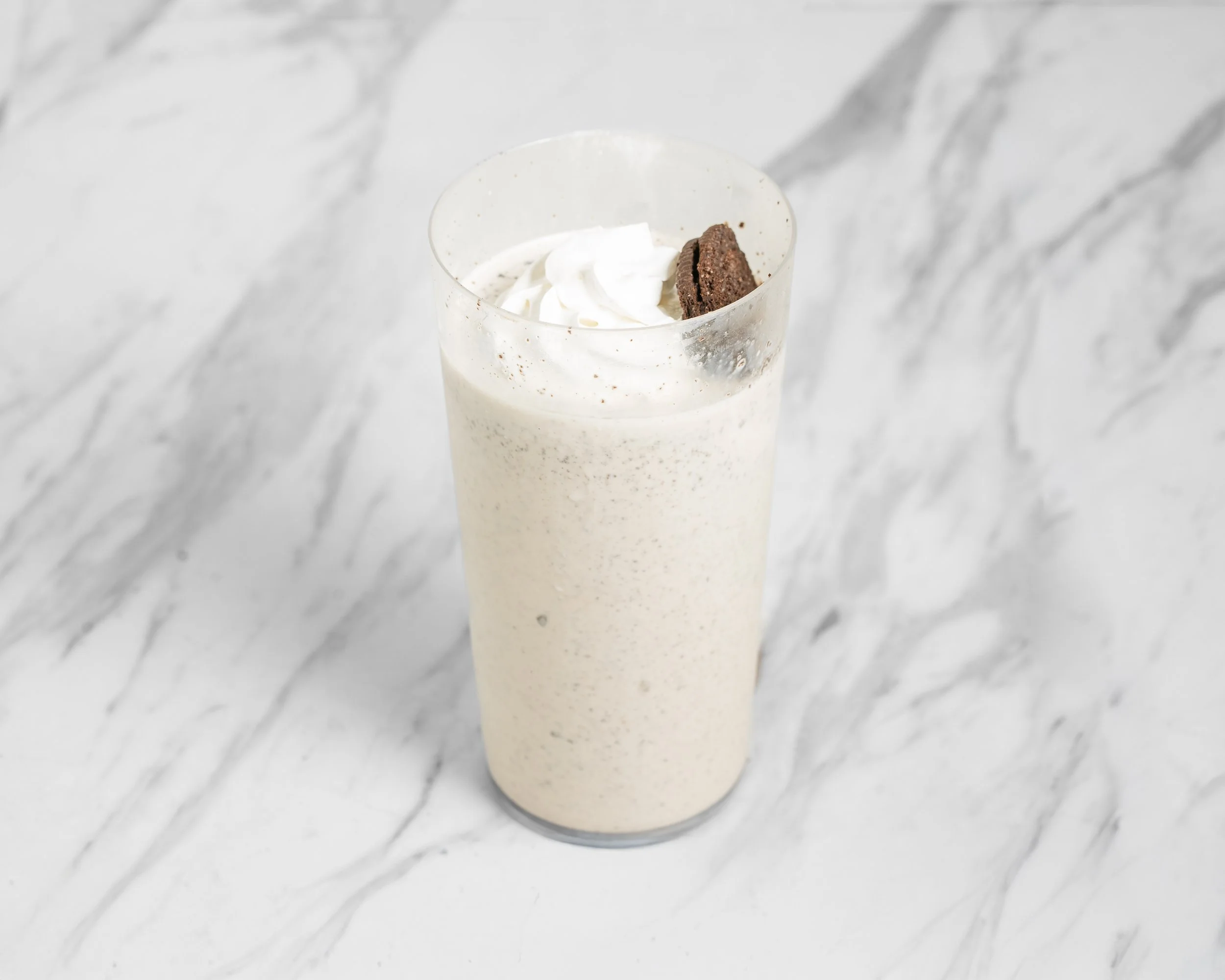 A glass of cookies and cream milkshake topped with whipped cream and a chocolate cookie