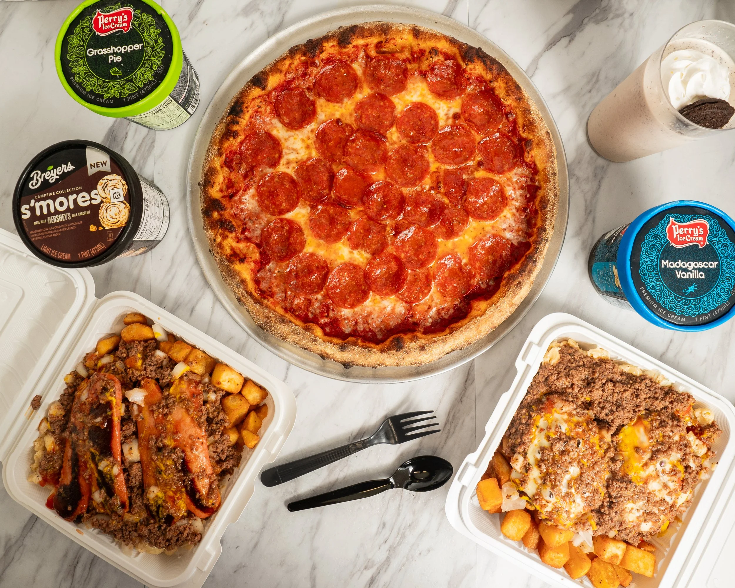 A pepperoni pizza on a white marble table, with two plastic containers of baked pasta dishes, two pint-sized ice cream containers (Grasshopper Pie, S'mores), a McDonald's sweet tea, a Perry's Madagascar Vanilla ice cream, and a black fork and spoon n