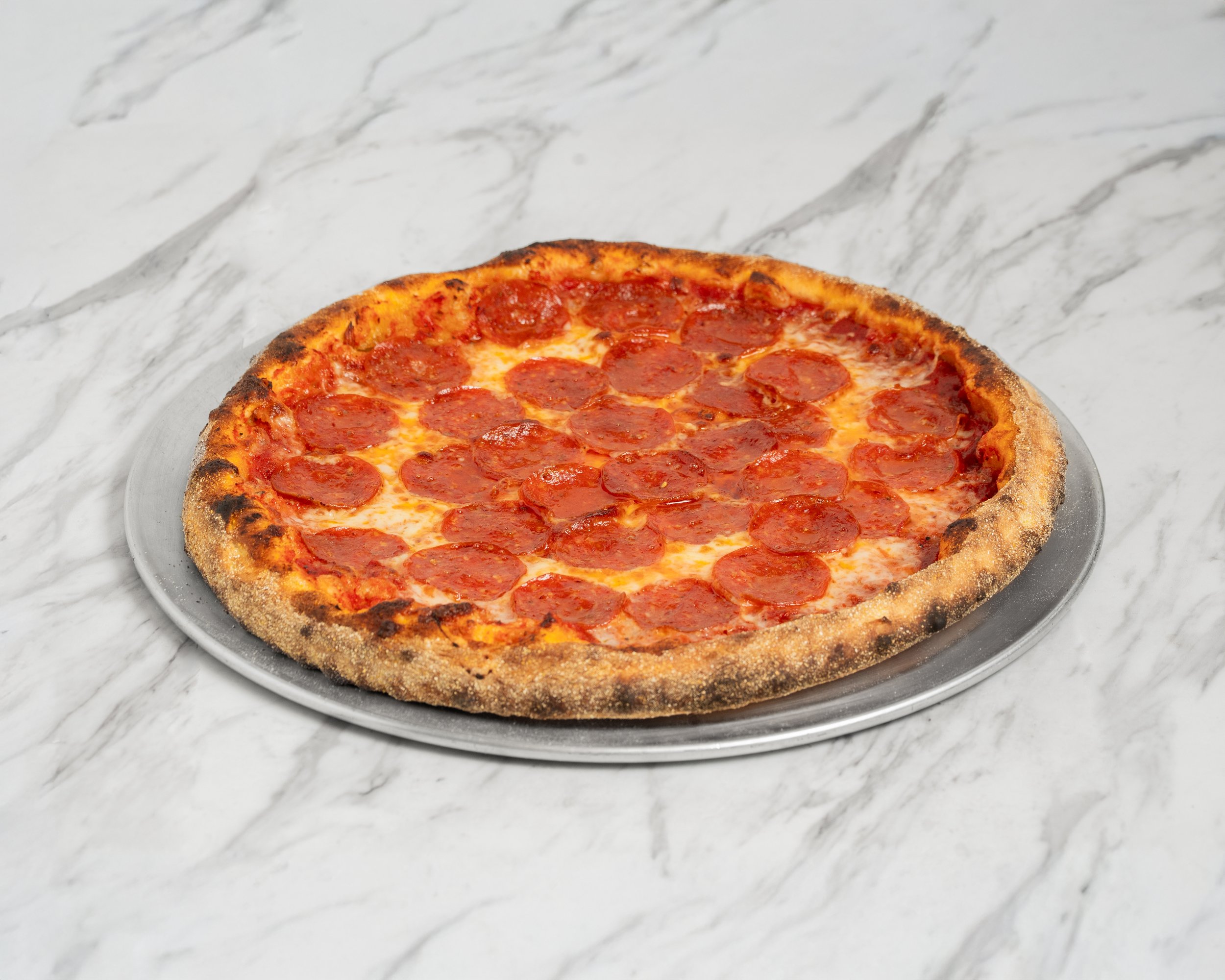 Pepperoni pizza on a metal tray on a marble countertop.