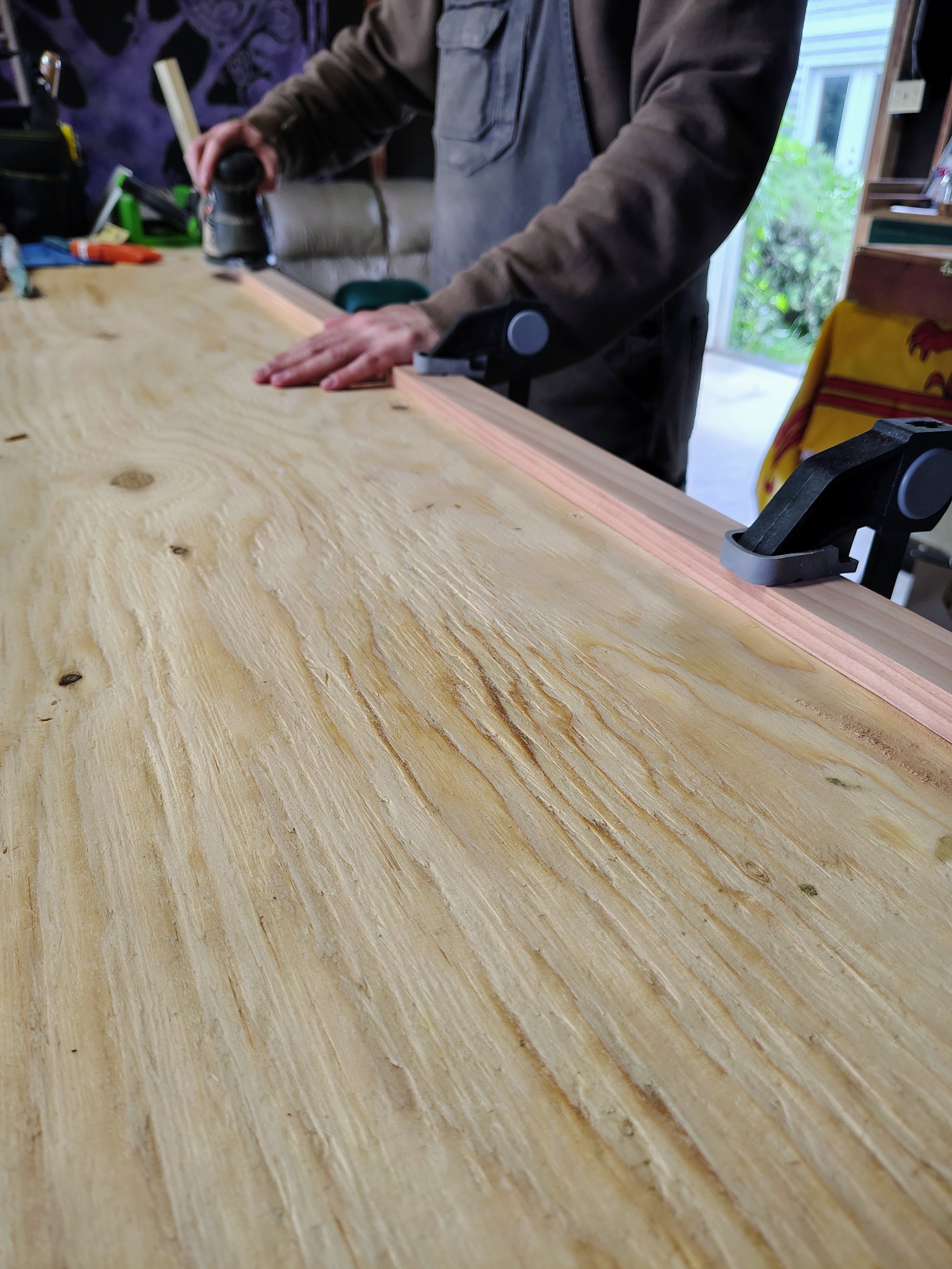 Person using a handheld electric sander to smooth a wooden surface in a workshop.
