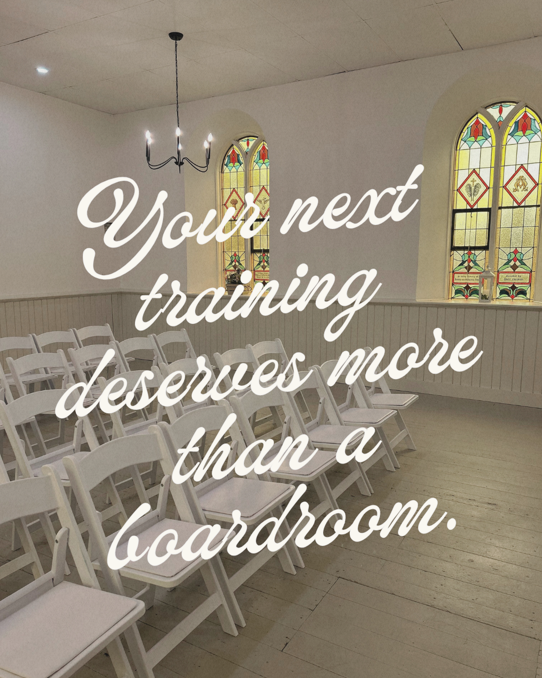 Empty room with white chairs arranged in rows, stained glass windows, a chandelier, and a wall with wainscoting. Overlaid text reading: 'You're next training desuues more than a boardroom.'