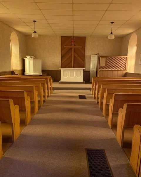 Empty church with wooden pews, an altar with a cross, and soft lighting.