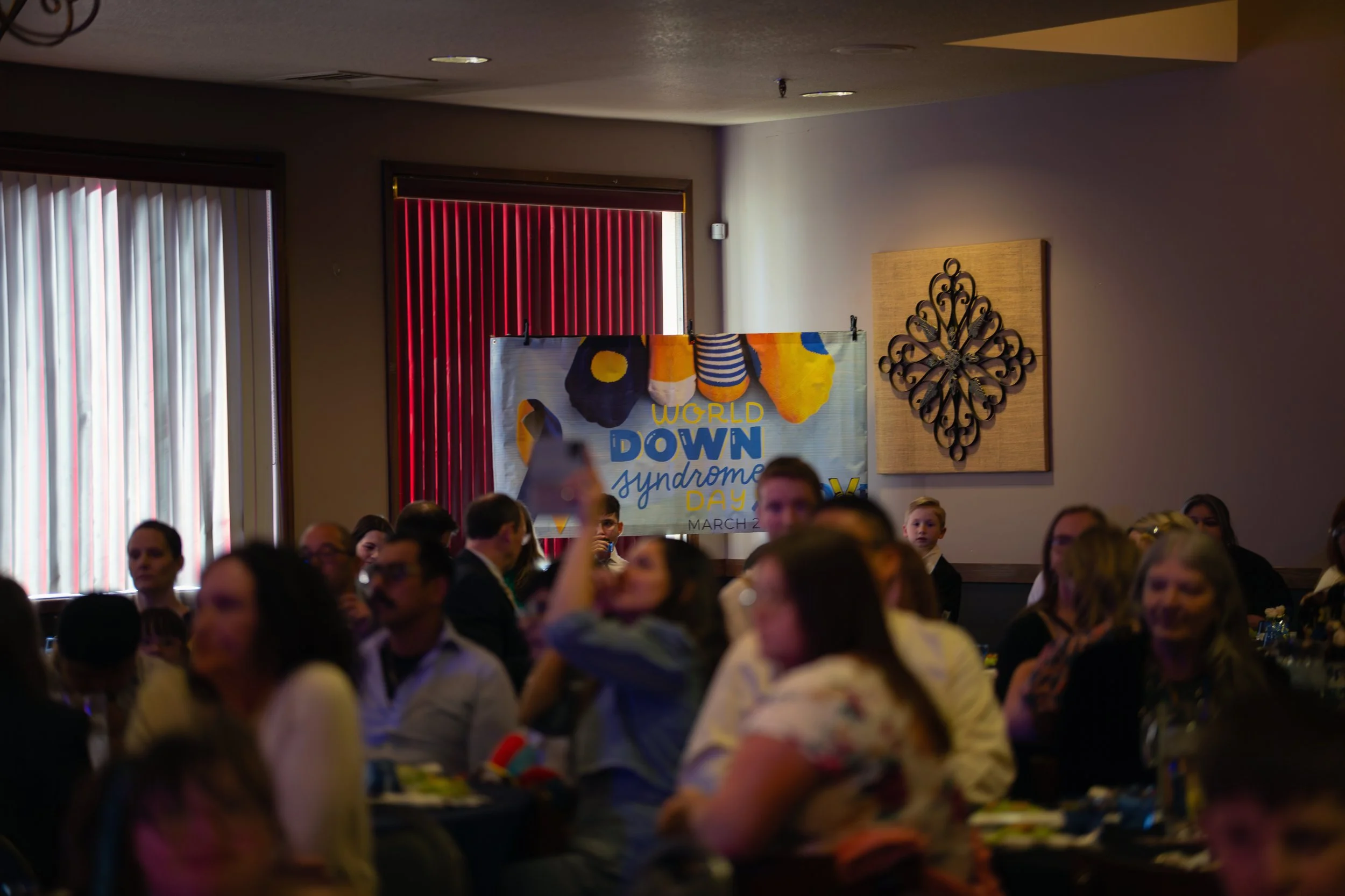 A Crowd of people in a room blurry with a focus on a banner for world down syndrome day