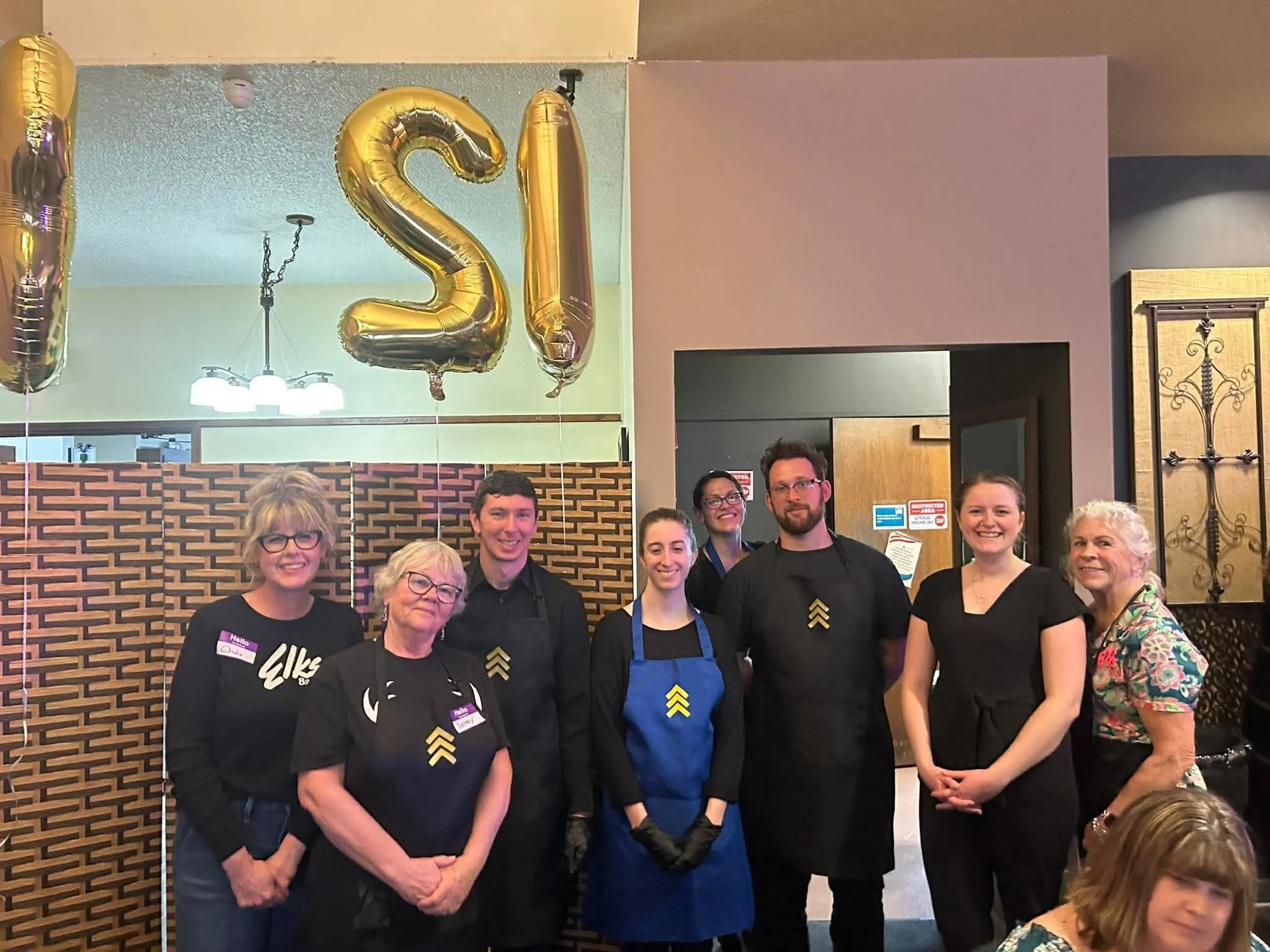 Group of volunteers wearing aprons standing together at the gala, smiling and supporting the event.