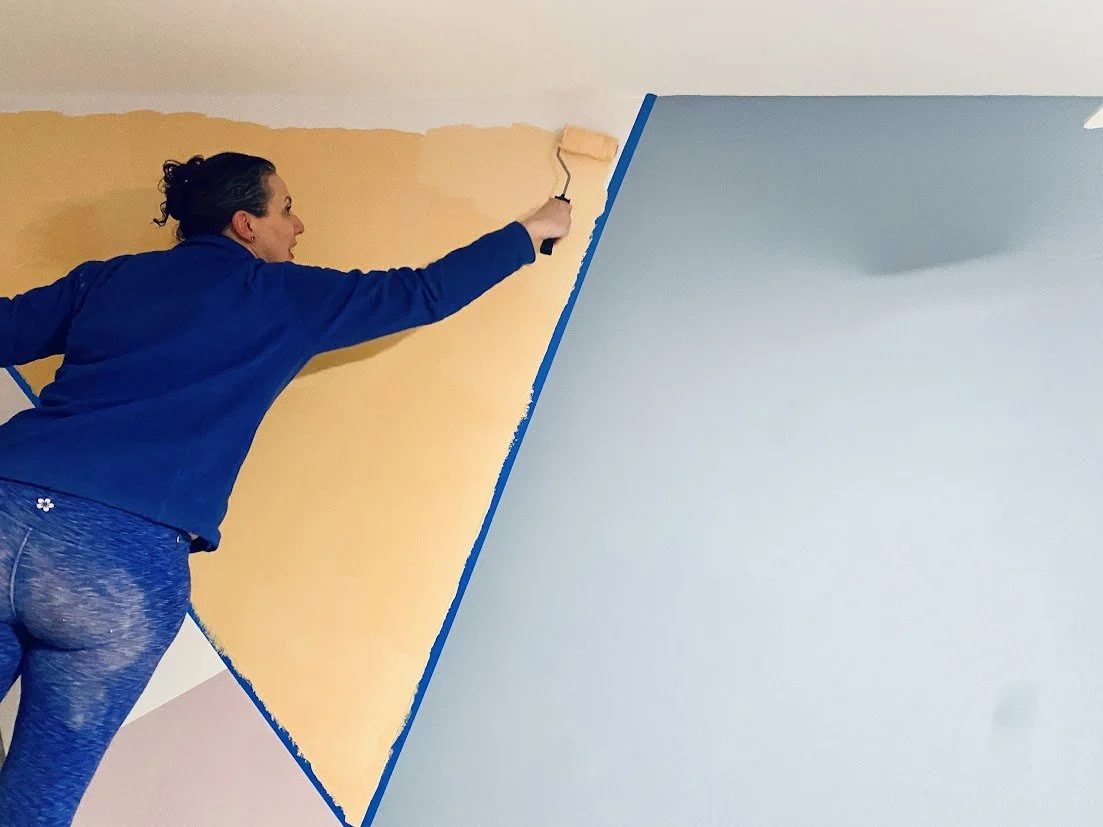 Pastel geometric mural in teal, peach, and navy with Studio Pearl artist Sarah Feinberg standing in front