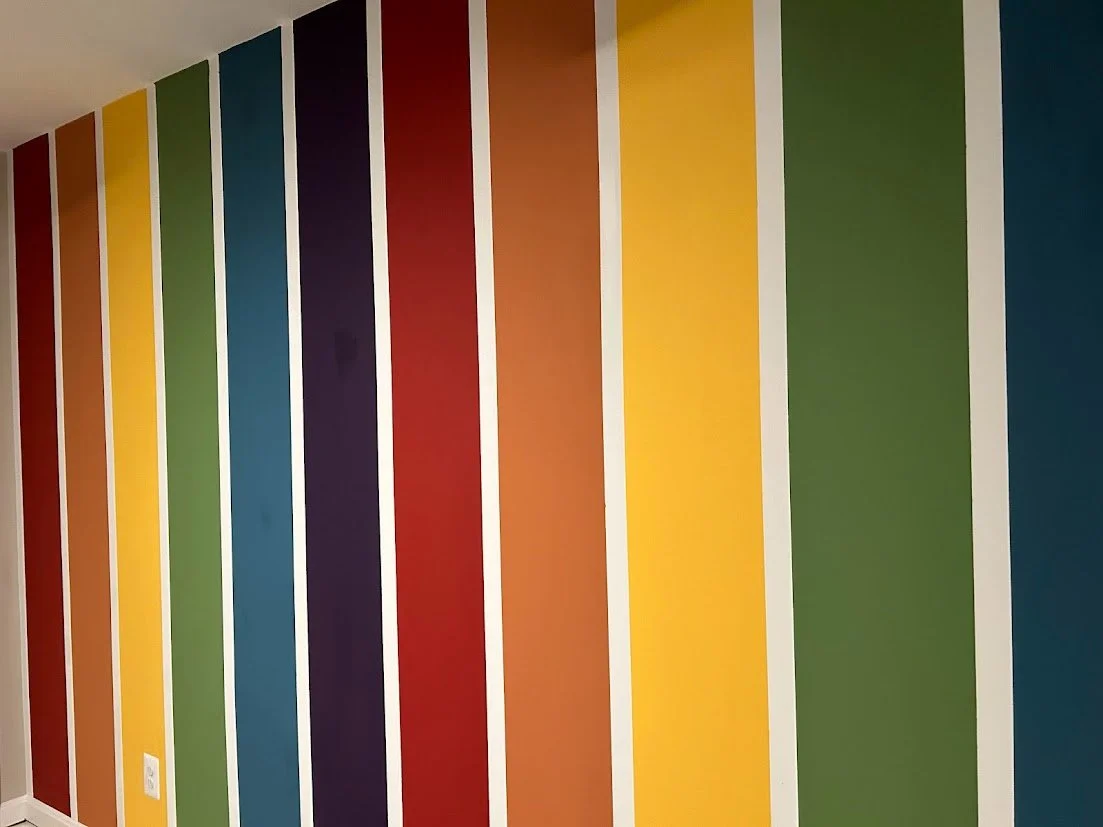 Floor-to-ceiling vertical stripe mural in rainbow colors, custom painted for a playroom accent wall