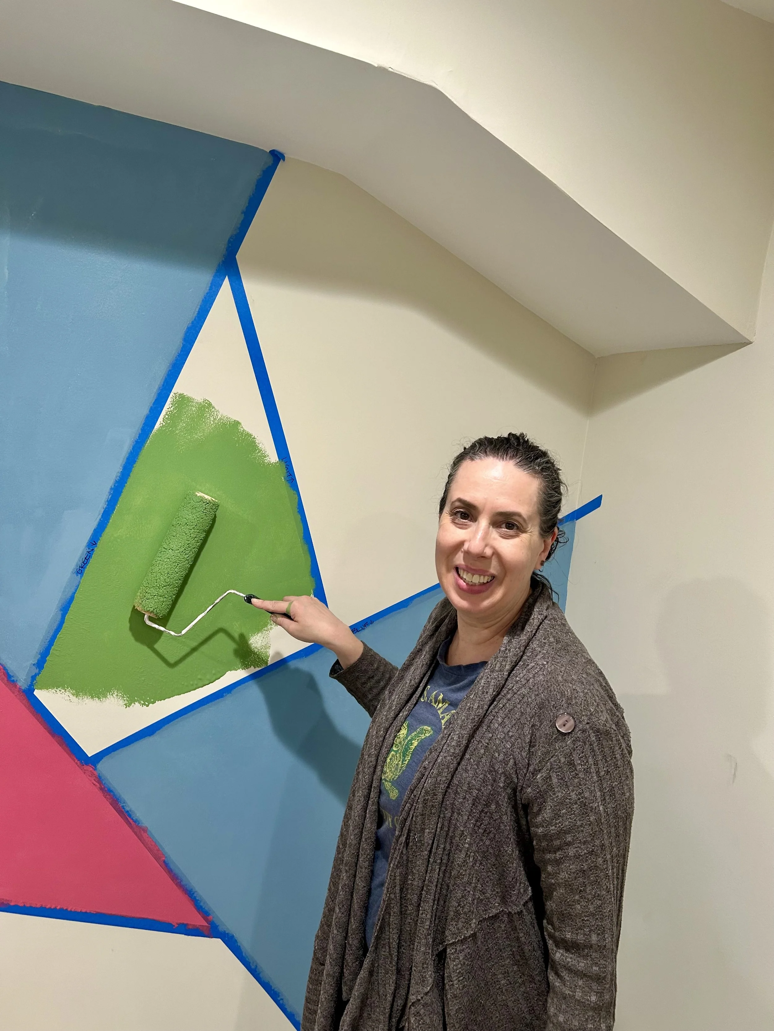 Sarah painting green paint of geometric, modern, abstract mural