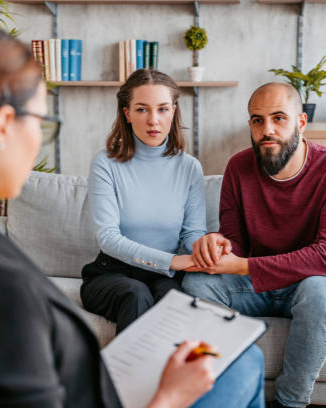 Couple sitting on a couch holding hands during therapy session with counselor taking notes.