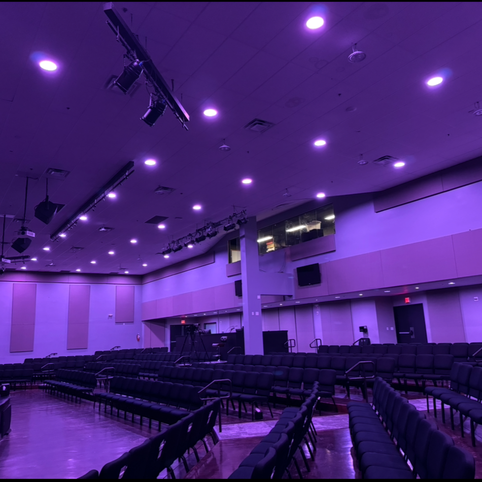 Empty auditorium with purple lighting, rows of black chairs, and stage lighting equipment