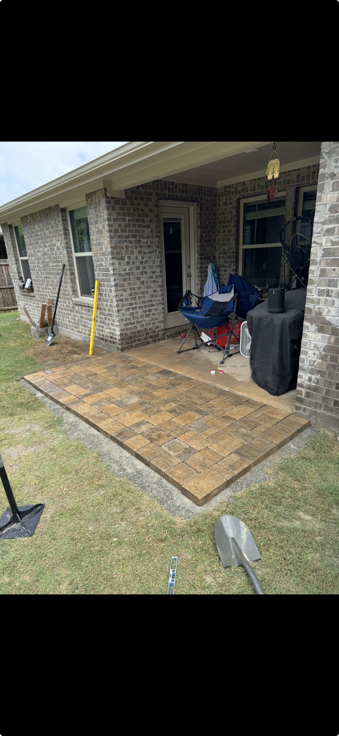 Back patio with brick pavers, patio furniture, tools, and a brick house wall.