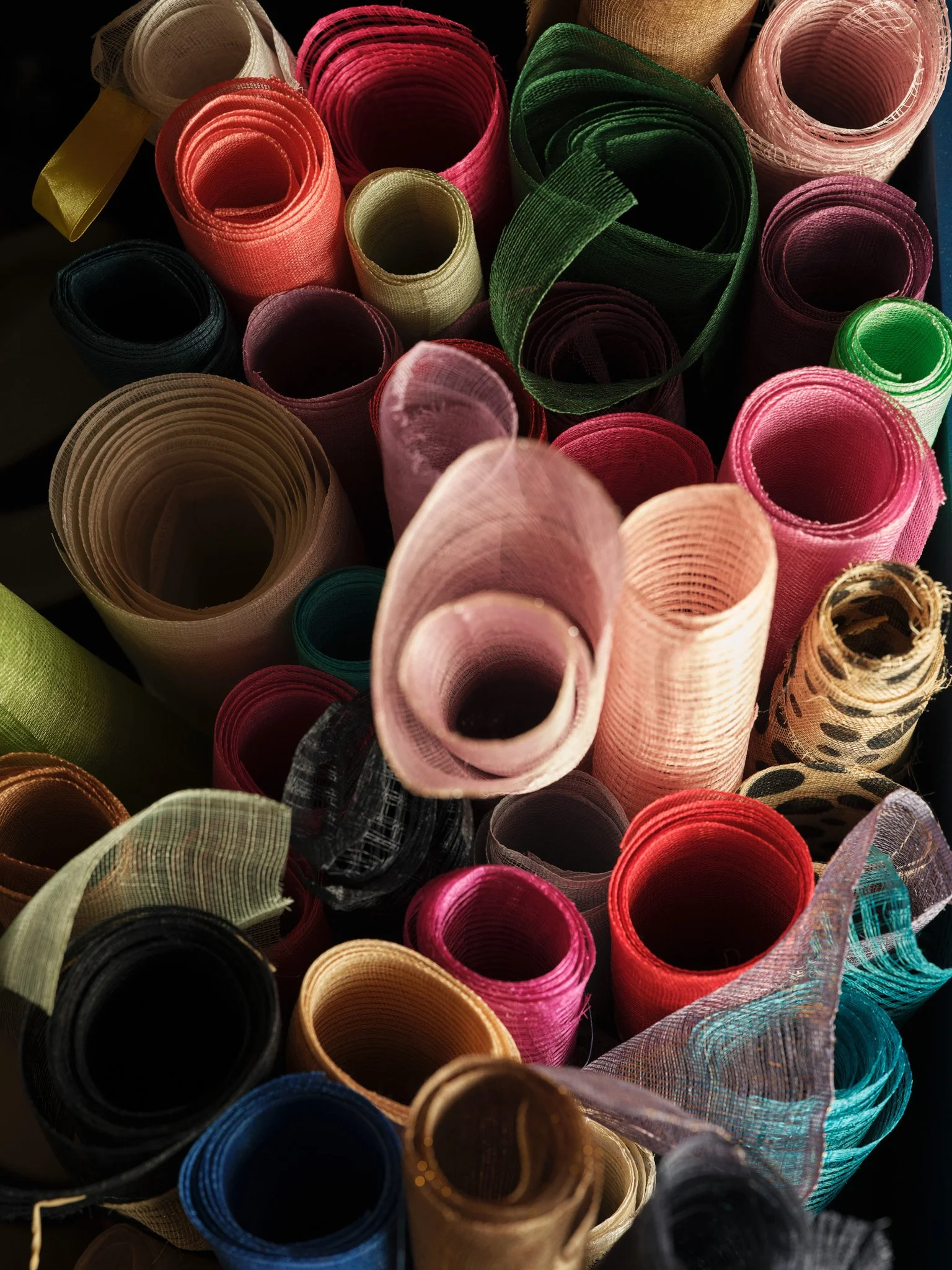Close-up of colorful rolls of ribbon, including pink, green, black, blue, gold, and patterns like leopard print, in a collection.