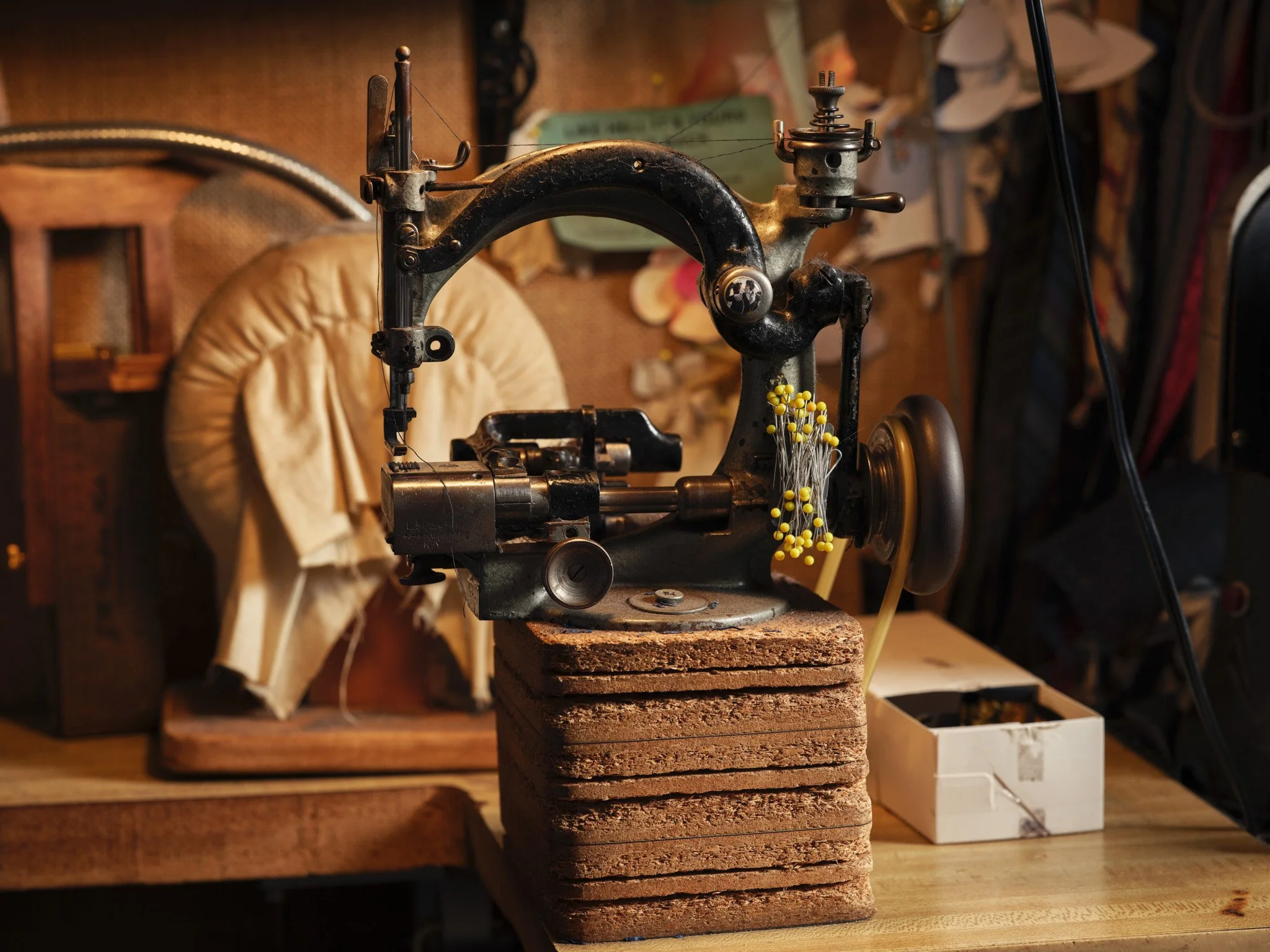 Vintage sewing machine on stacked bricks in a workshop surrounded by fabric, paper, and other sewing supplies.