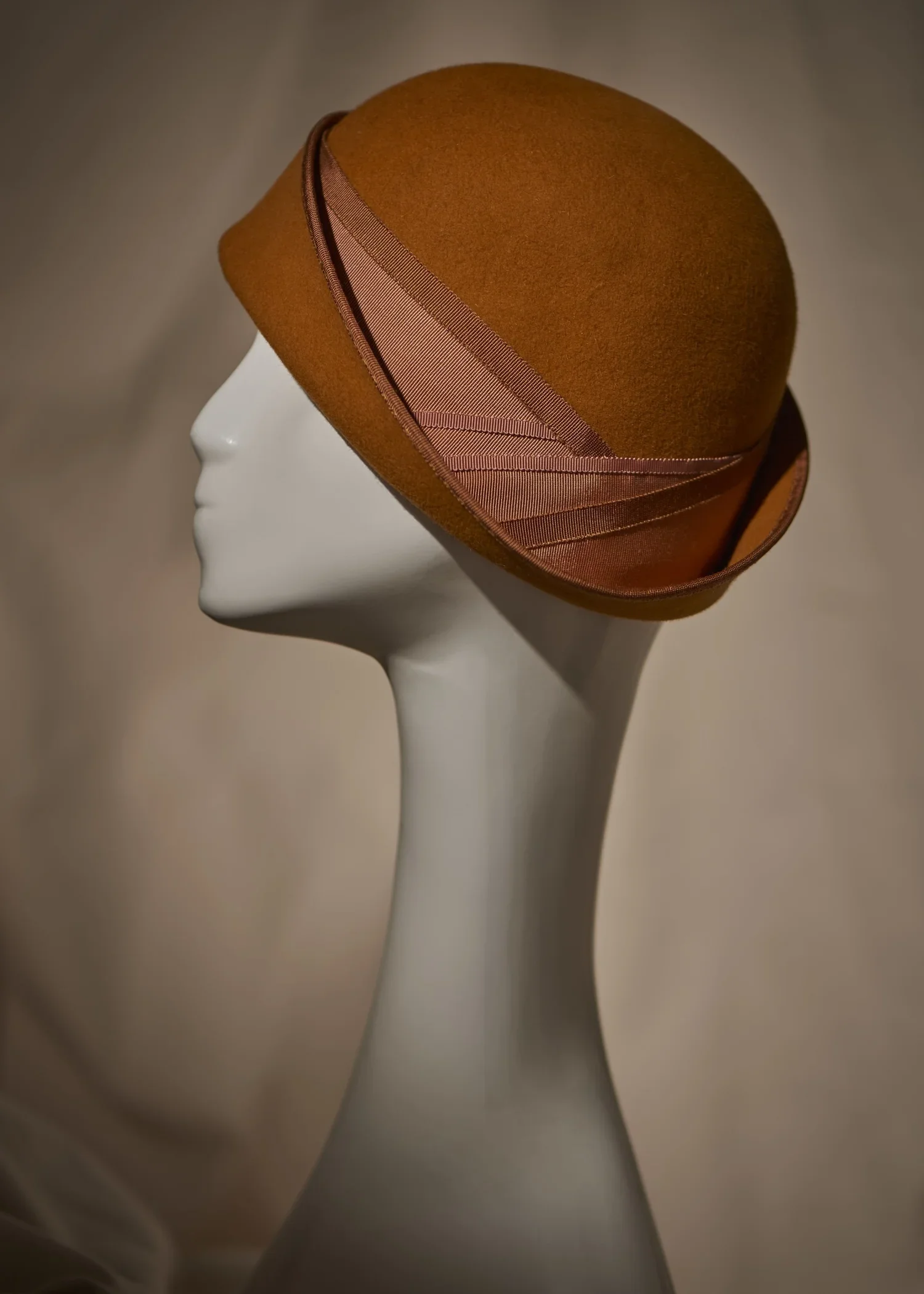 A tan or brown felt hat with pink ribbon embellishment displayed on a white mannequin head against a neutral background.