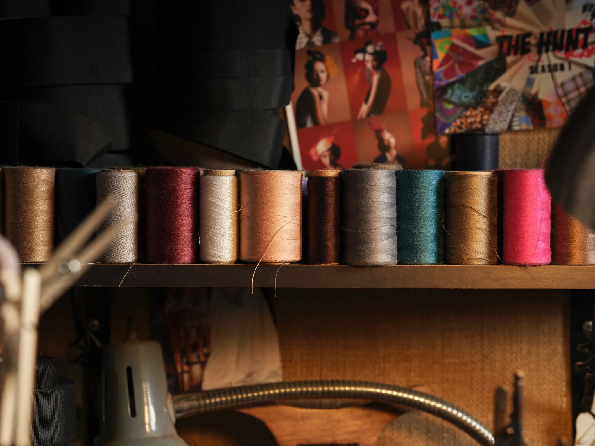 Photo of a row of colorful sewing threads on a shelf, with patches of fabric and posters in the background.