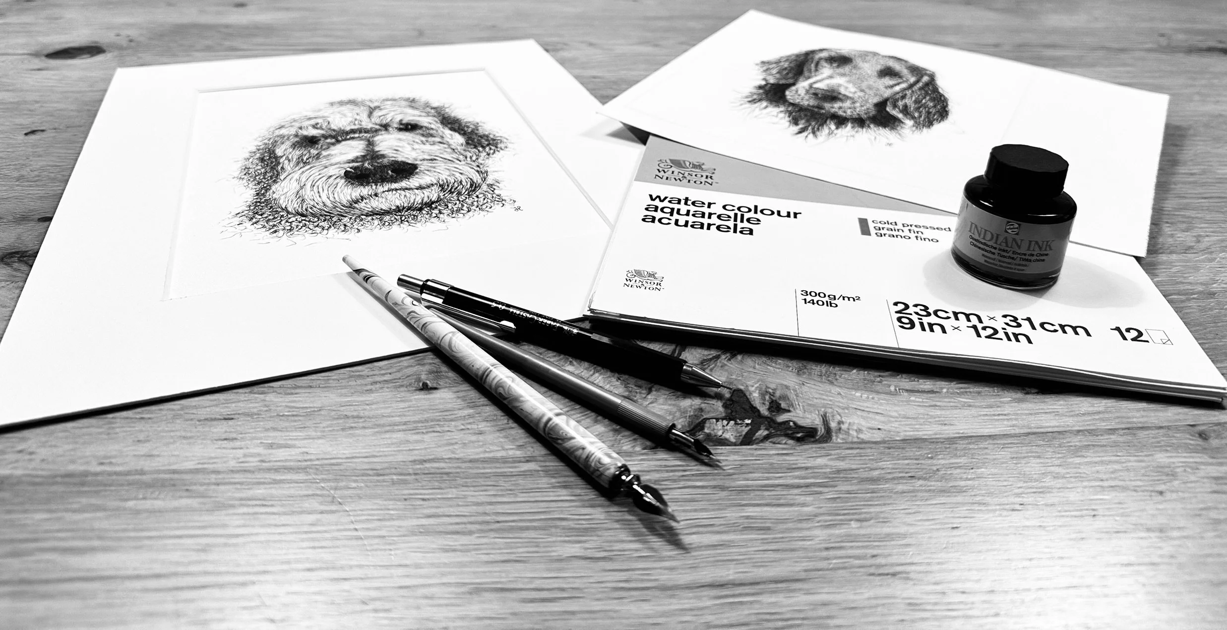 A sketch of a dog's face on white paper, watercolor painting supplies, and art tools on a wooden table.