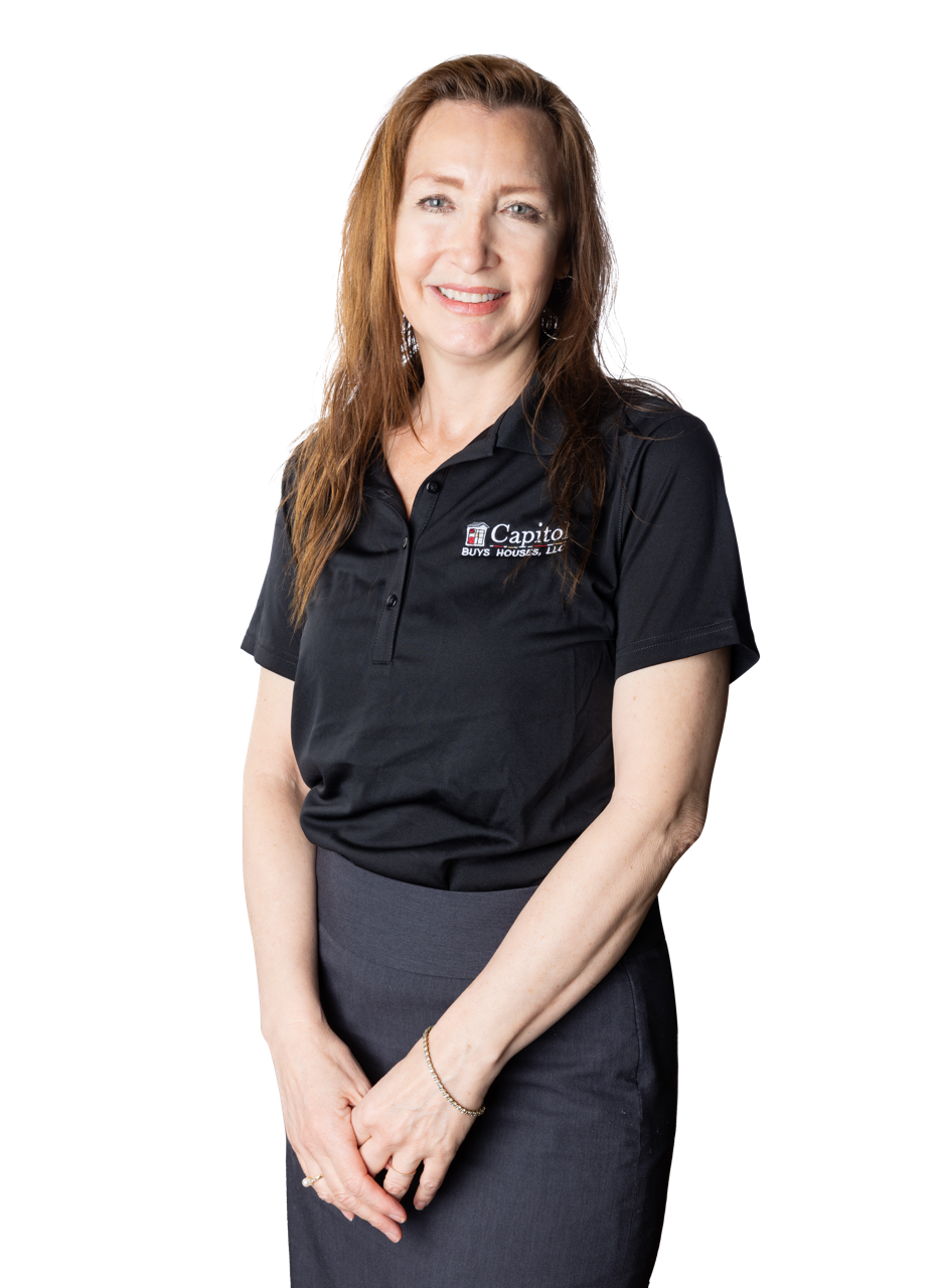 A woman with long red hair wearing a black polo shirt with a company logo and a gray skirt, standing against a plain background.
