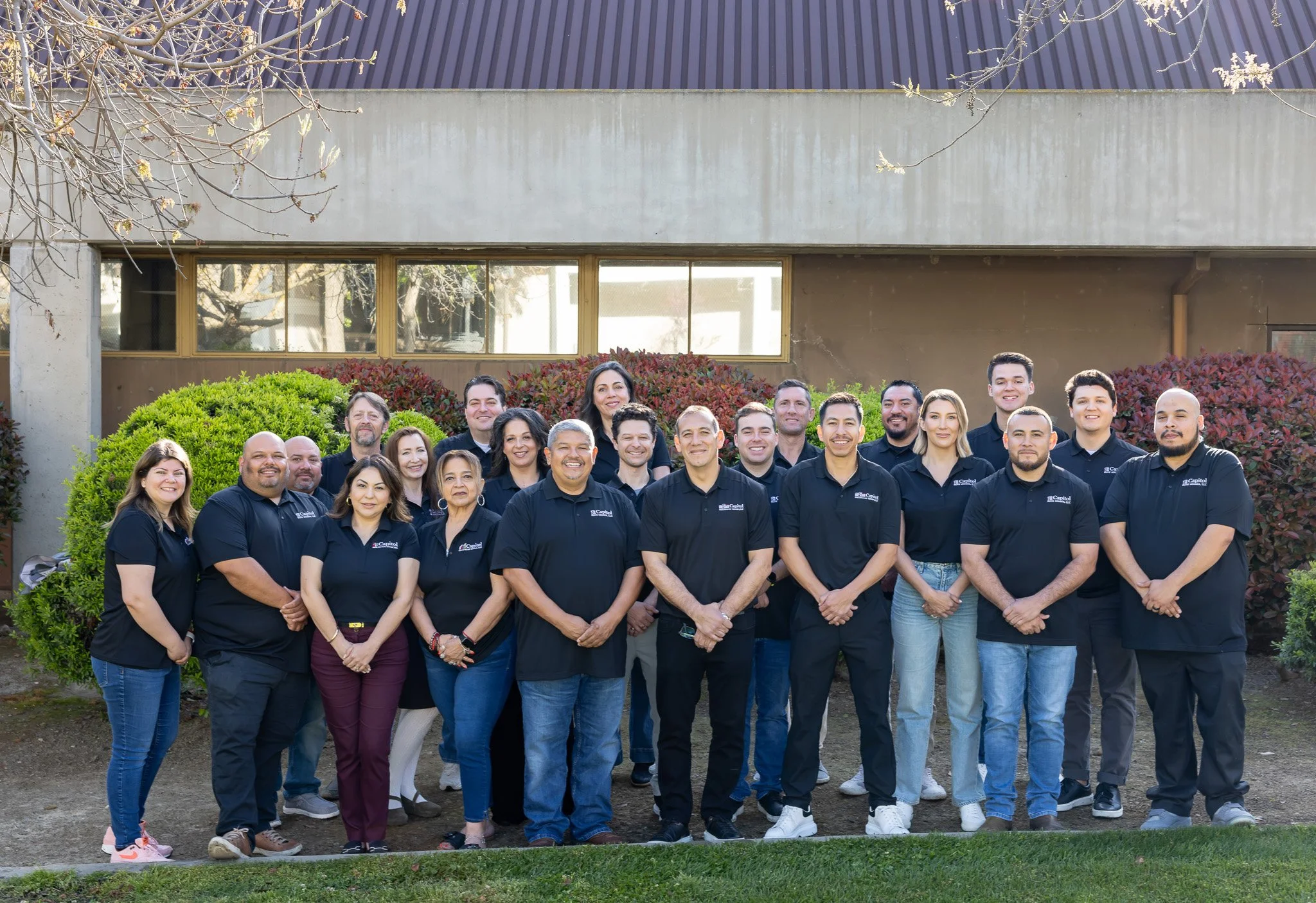 The team over 20 people at Capitol Real Estate Group, standing shoulder to shoulder in front of a building.