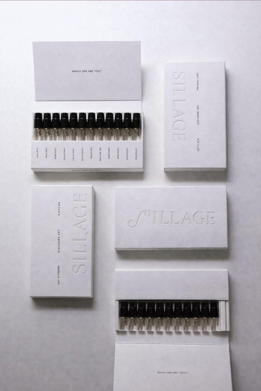 Set of white boxes and glass vials with black caps, arranged on a white surface, with embossed and printed text.