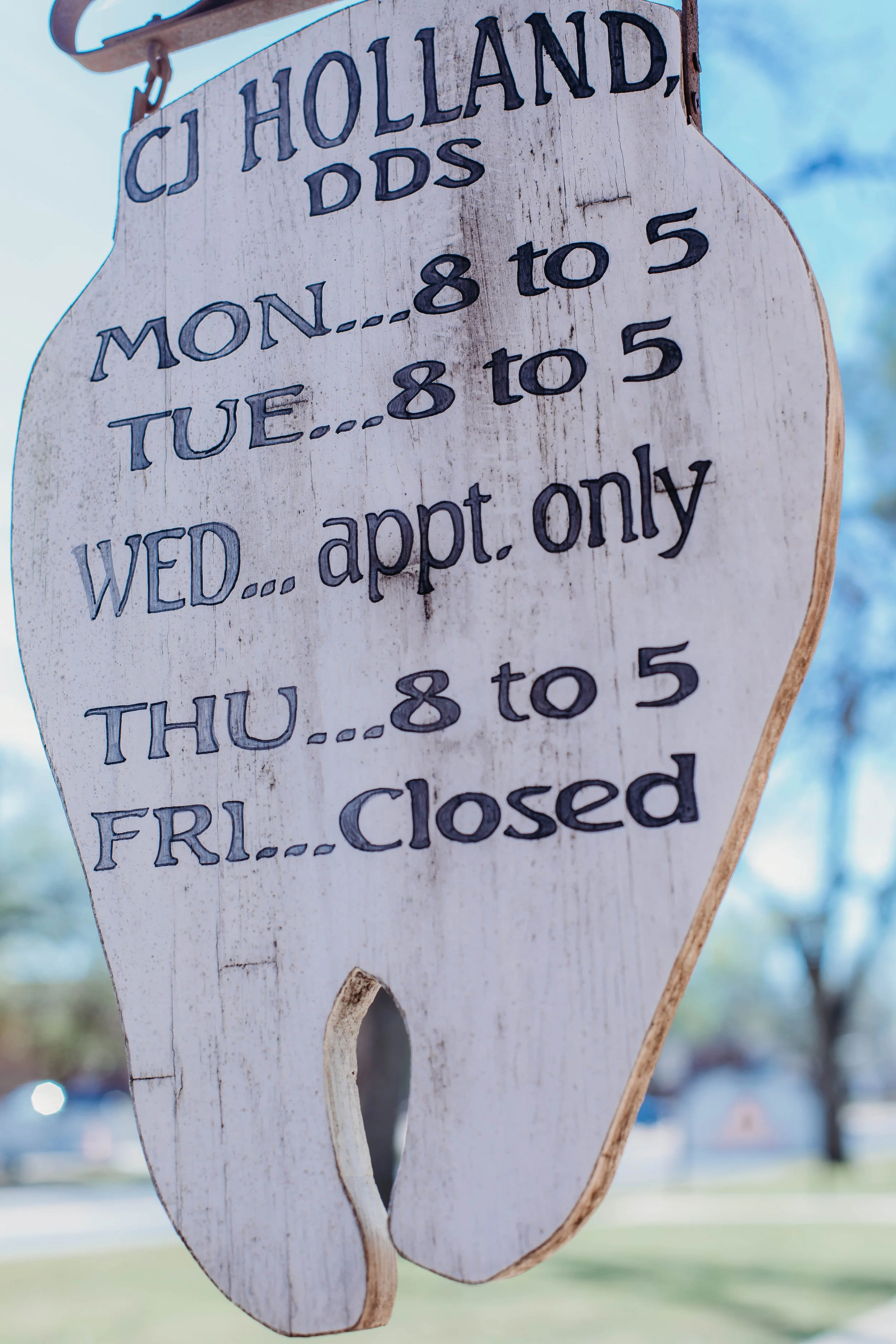 Wood sign with business hours, hanging outdoors with a blue sky in the background.