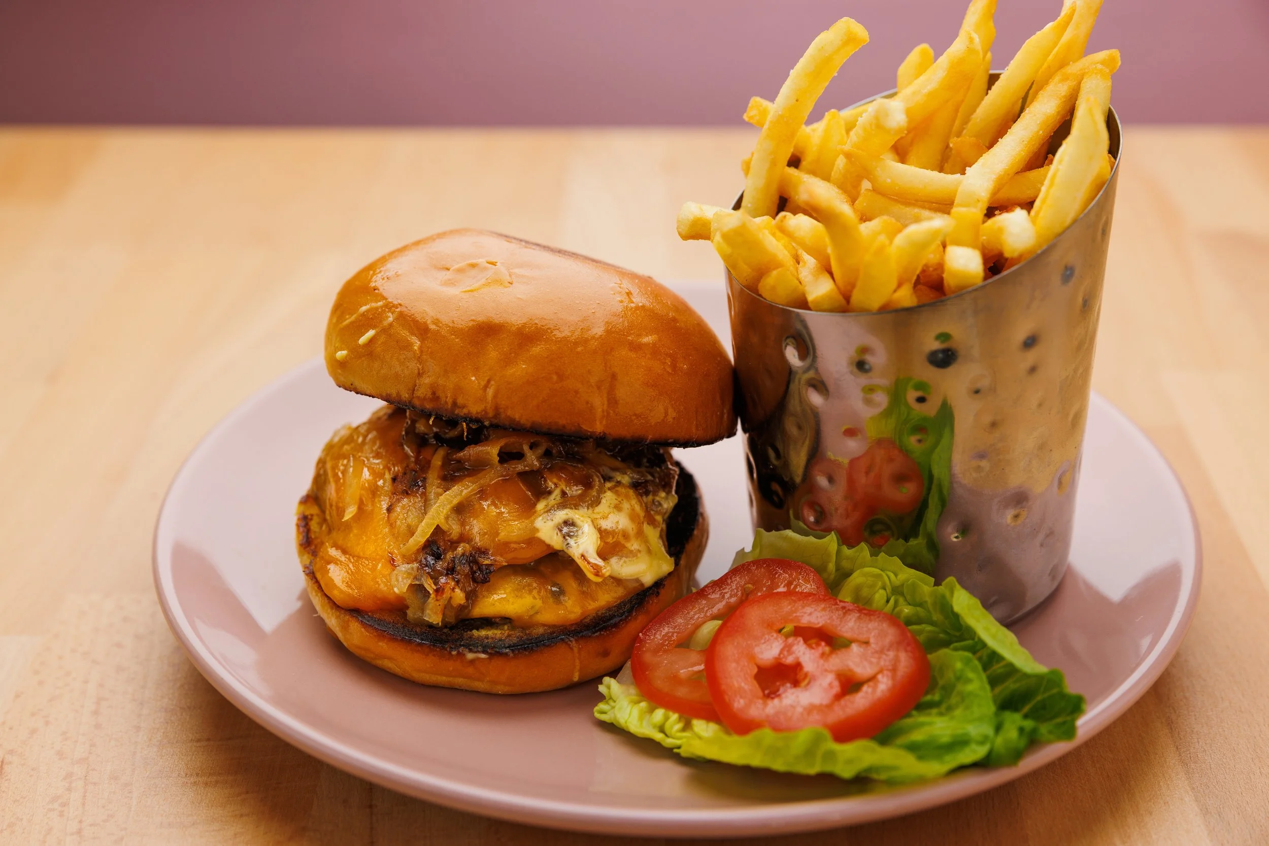 Cheeseburger with fries and sliced tomatoes and lettuce on a pink plate.