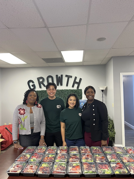 Four Meals 50 people standing behind a table of packed salads in a room with a sign that says "GROWTH" on the wall.
