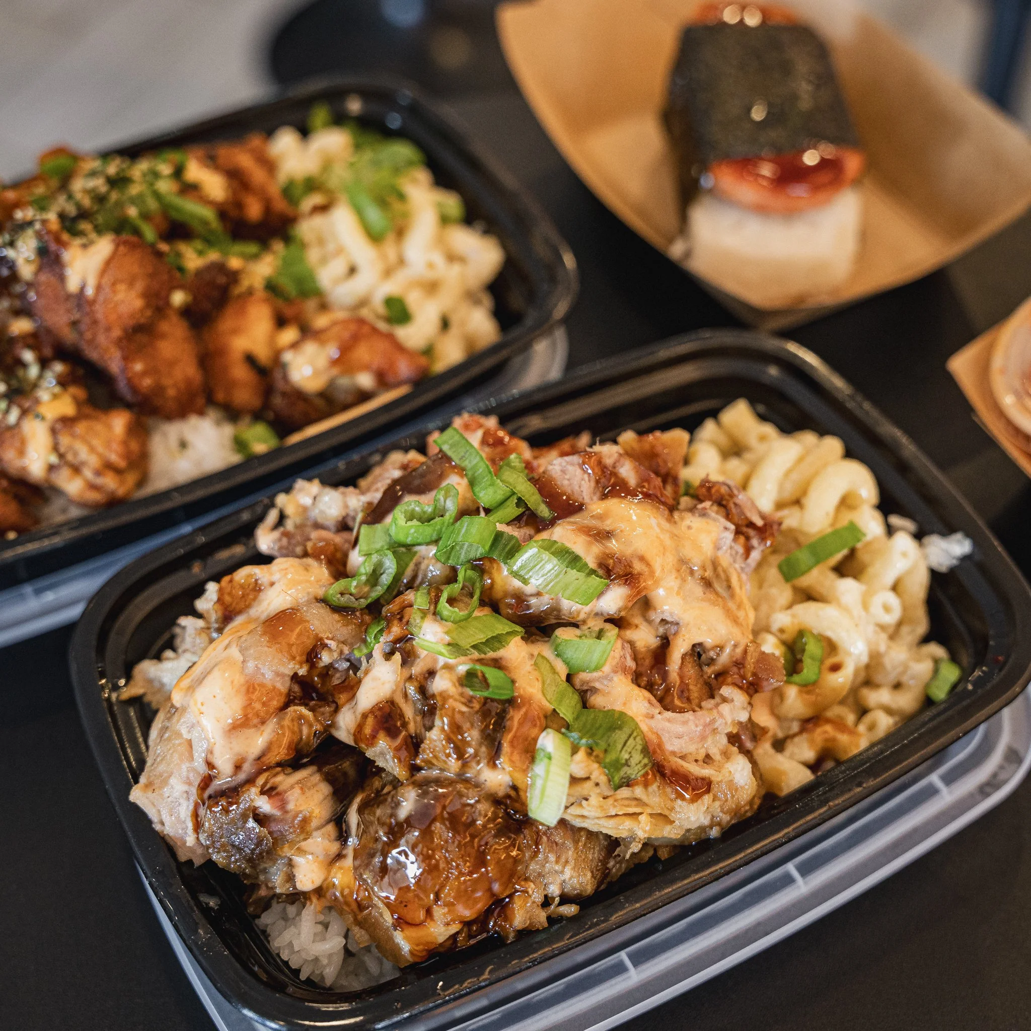 Close-up of a sushi bento box containing rice, cooked chicken topped with chopped green onions, with slices of grilled eel covered in sauce, and macaroni salad.