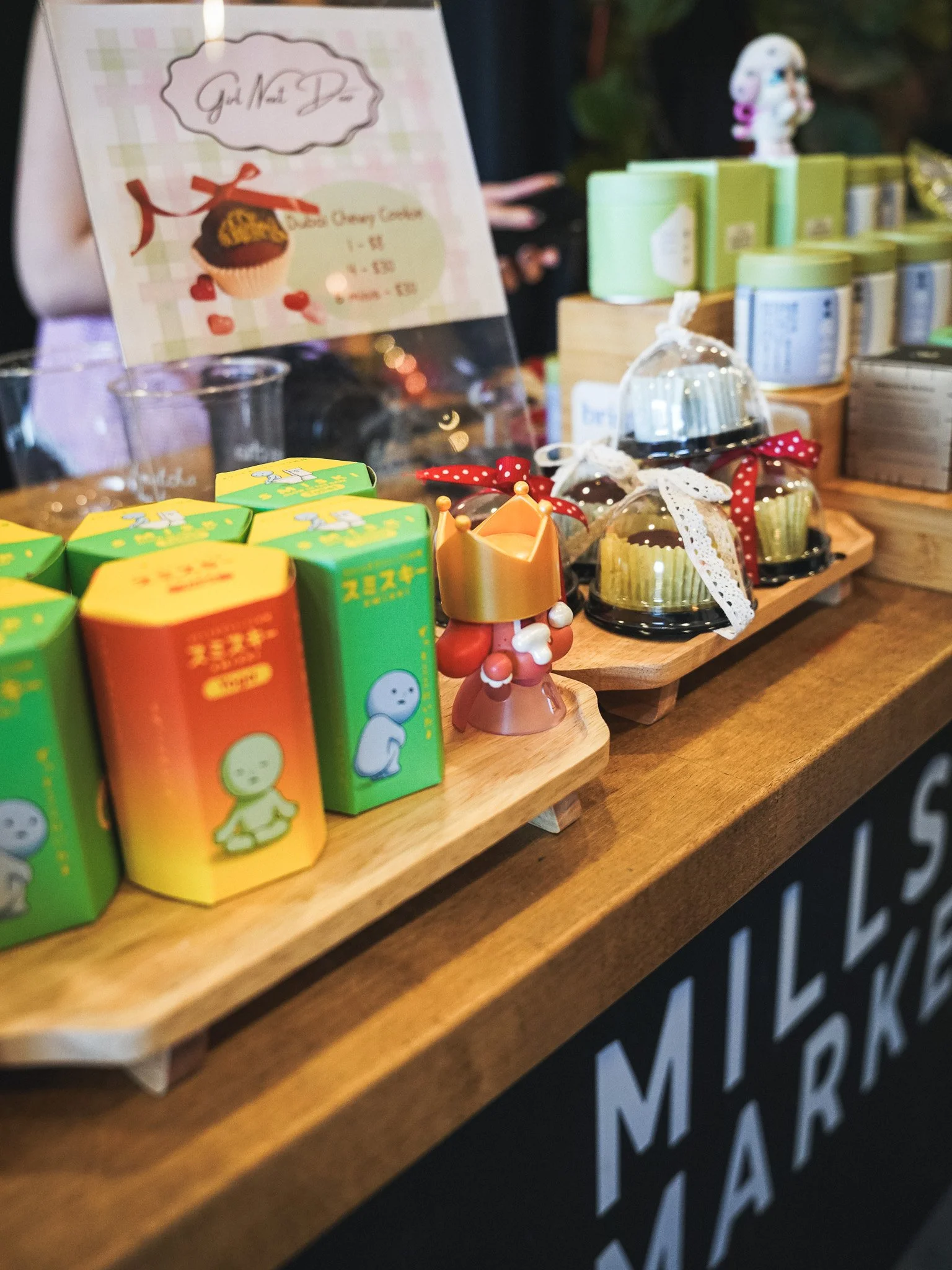 Display of colorful tea boxes and desserts with a menu board in the background at a market or shop.