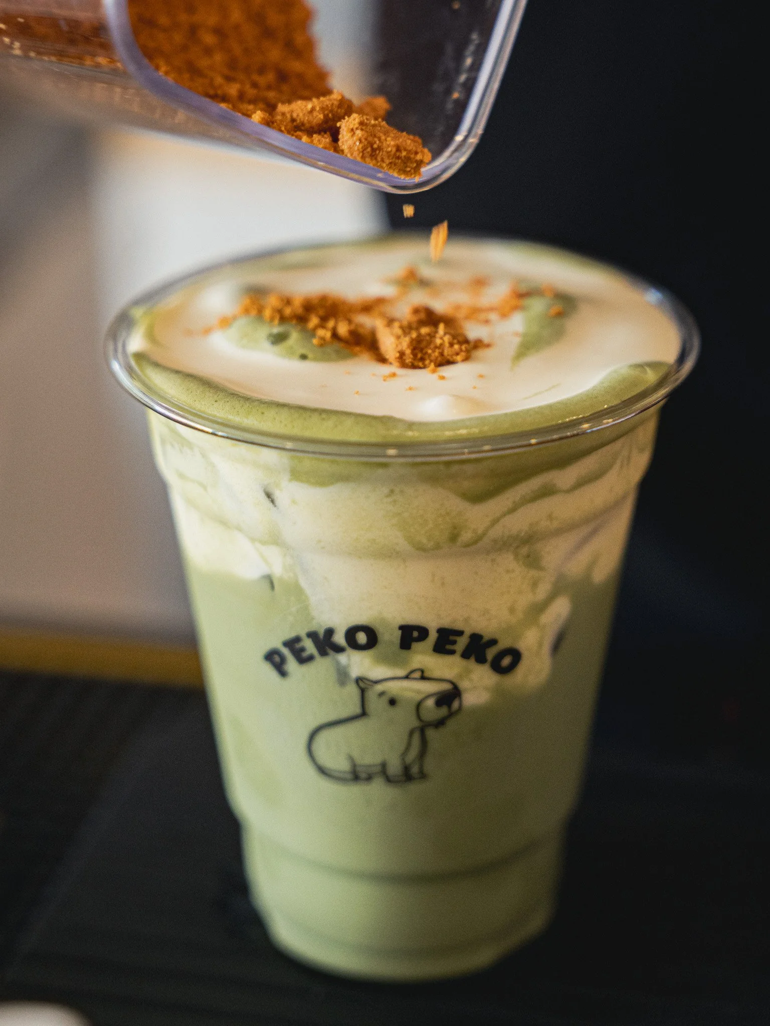Close-up of an ice cream or beverage cup with a bear logo, green and white swirled design, and crushed cookies or crumbs on top.