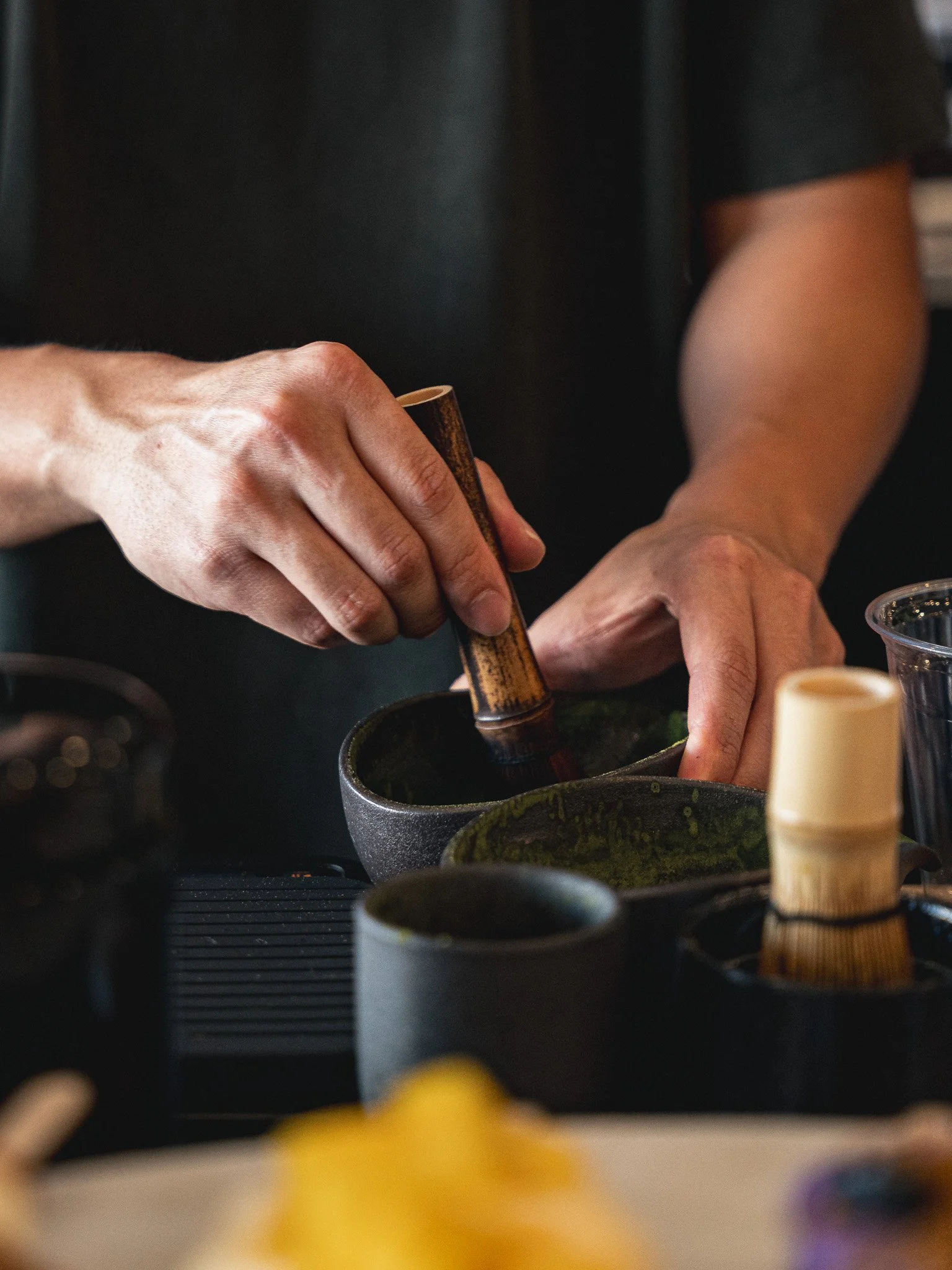 Close-up of a person pressing a button or grinding, with various kitchen or culinary tools and containers in the background.