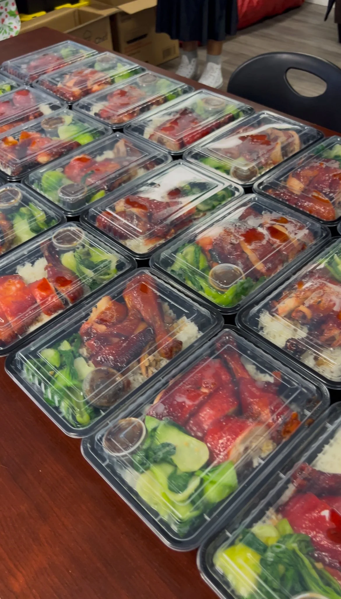 Pre-packaged meals with rice, vegetables, and meat covered with plastic lids on a wooden table.