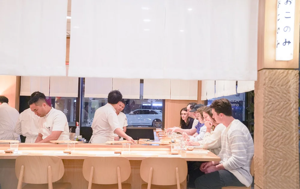 People dining at Okonomi counter with chefs preparing food