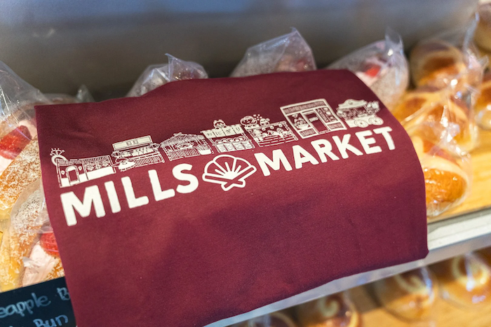 mills-market-maroon-t-shirt-merchandise-folded-near-bakery-pastries.png