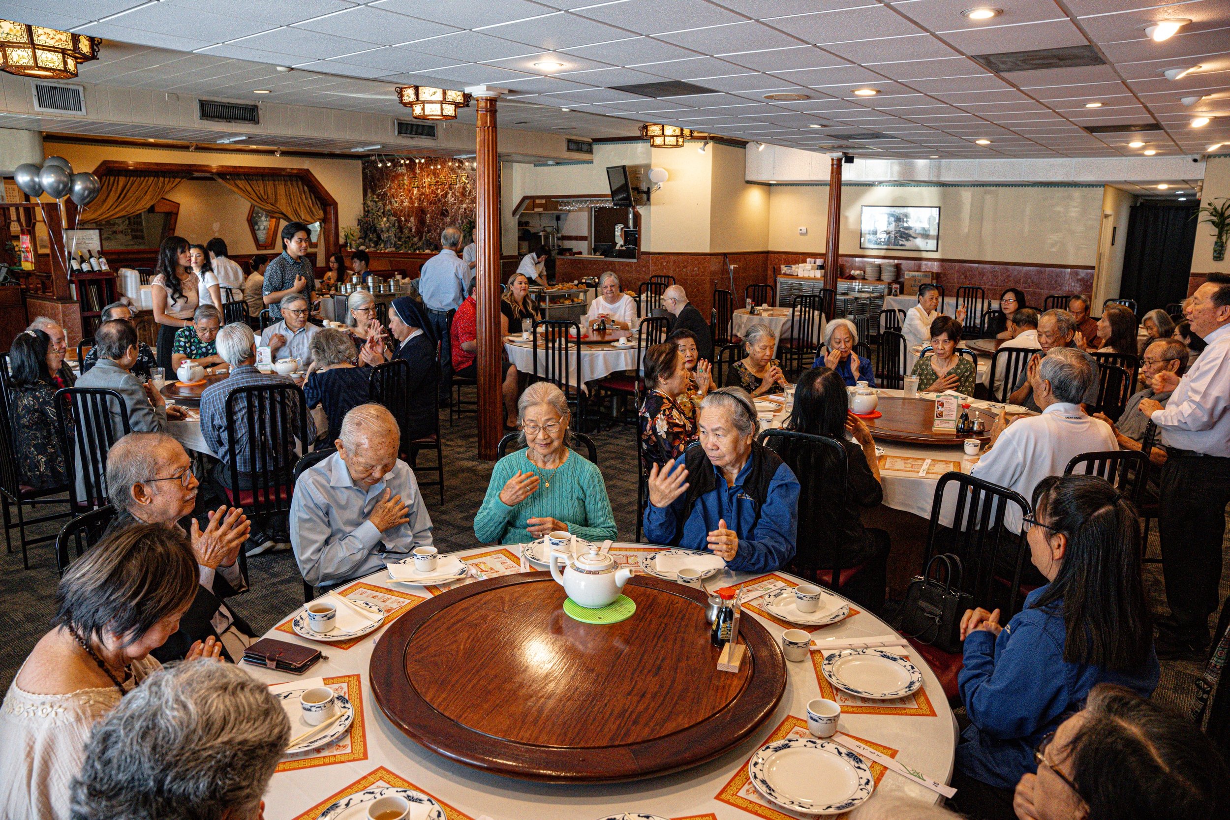 Restaurant filled with senior citizens having lunch at large round tables. 