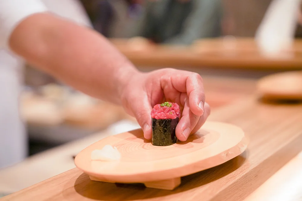 A person placing a piece of sushi on a wooden plate at Okonomi.