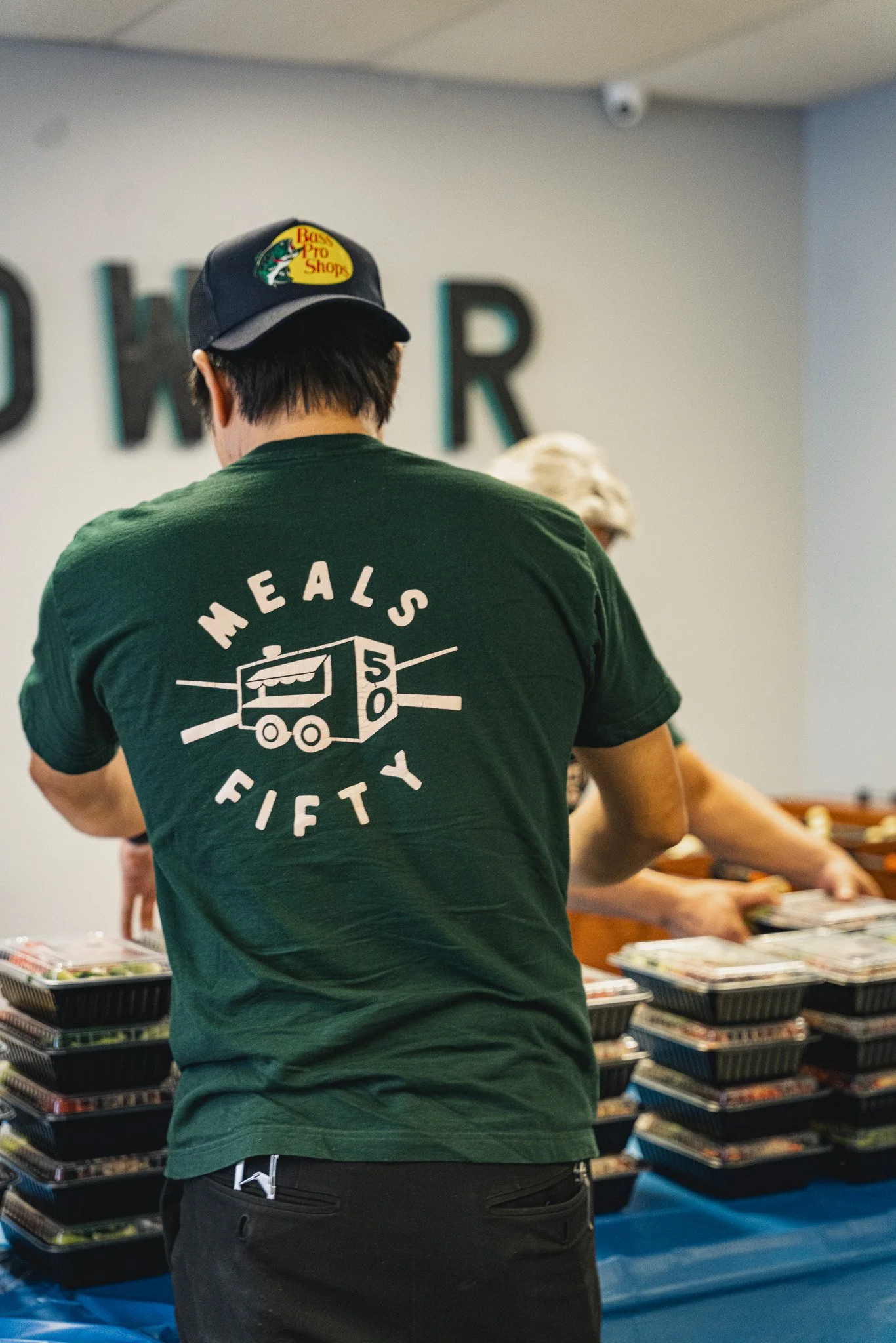backside of meals 50 team member wearing hat and green shirt arranging a table of hot boxed meals