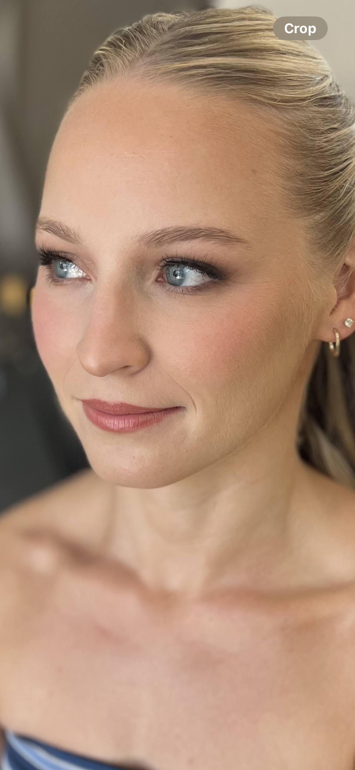Close-up of a smiling woman with blonde hair, blue eyes, and pierced ears, looking slightly to the right, with natural makeup.